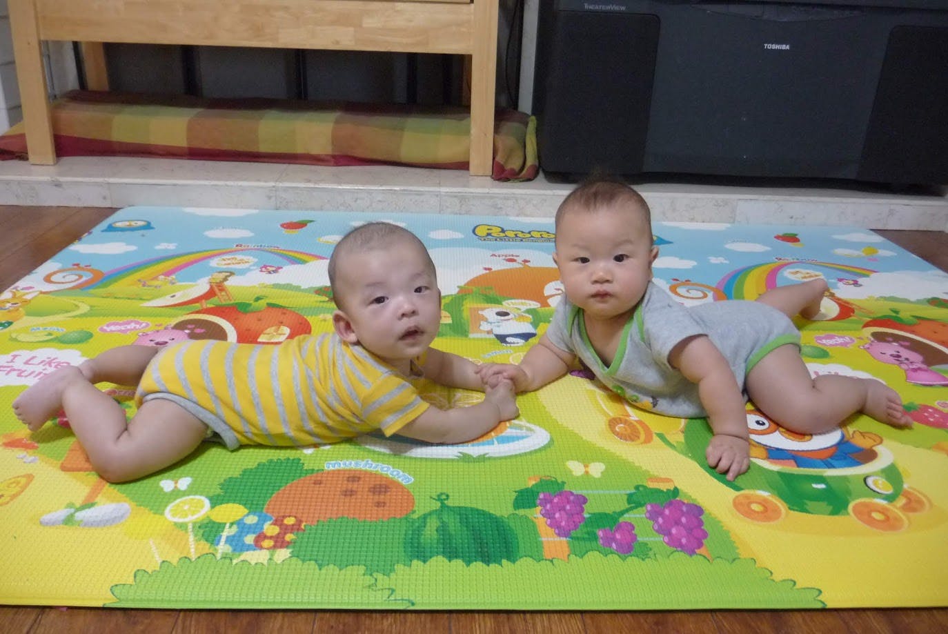 Two babies crawling on a colorful playmat