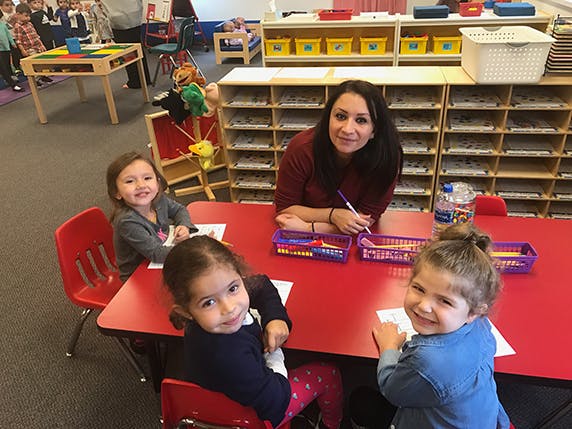 Adult and three children sitting at a red table in a classroom