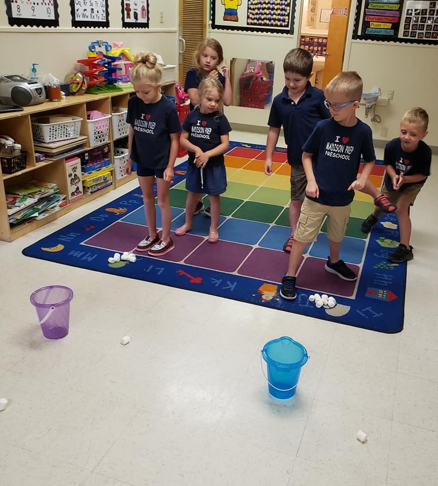 Children playing a game with buckets and small white balls on a colorful rug