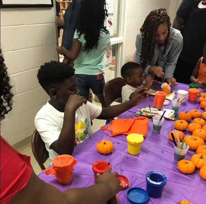 People and children painting small pumpkins at a table