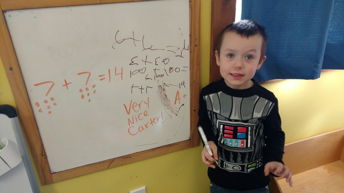 Child holding a marker next to a whiteboard with math problems