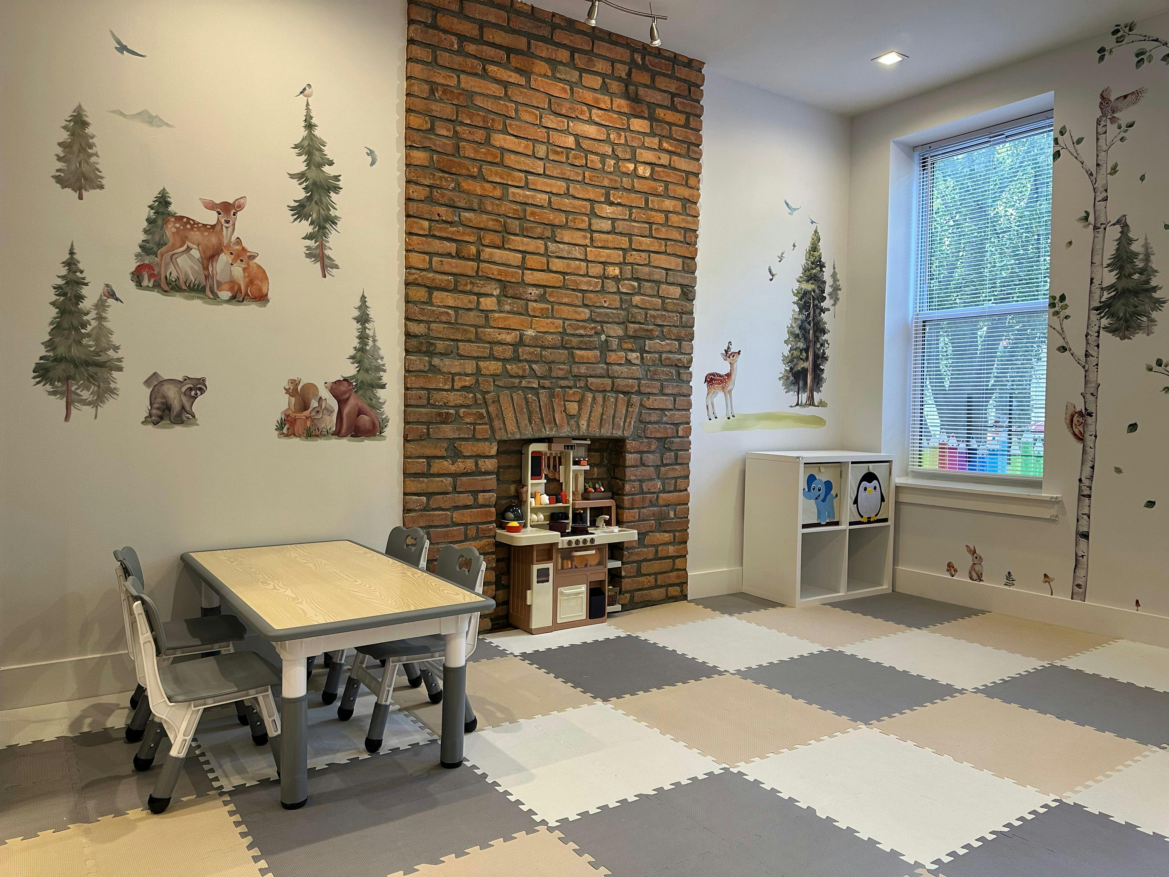 Playroom with small table and chairs, brick fireplace, and nature-themed wall decals