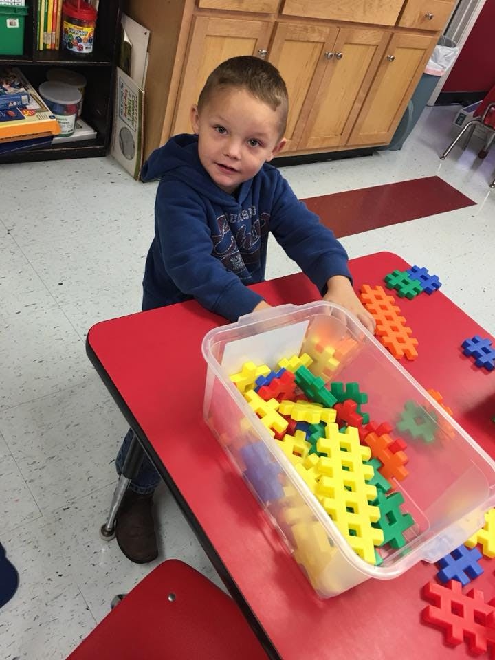 Child playing with colorful interlocking building blocks on a red table