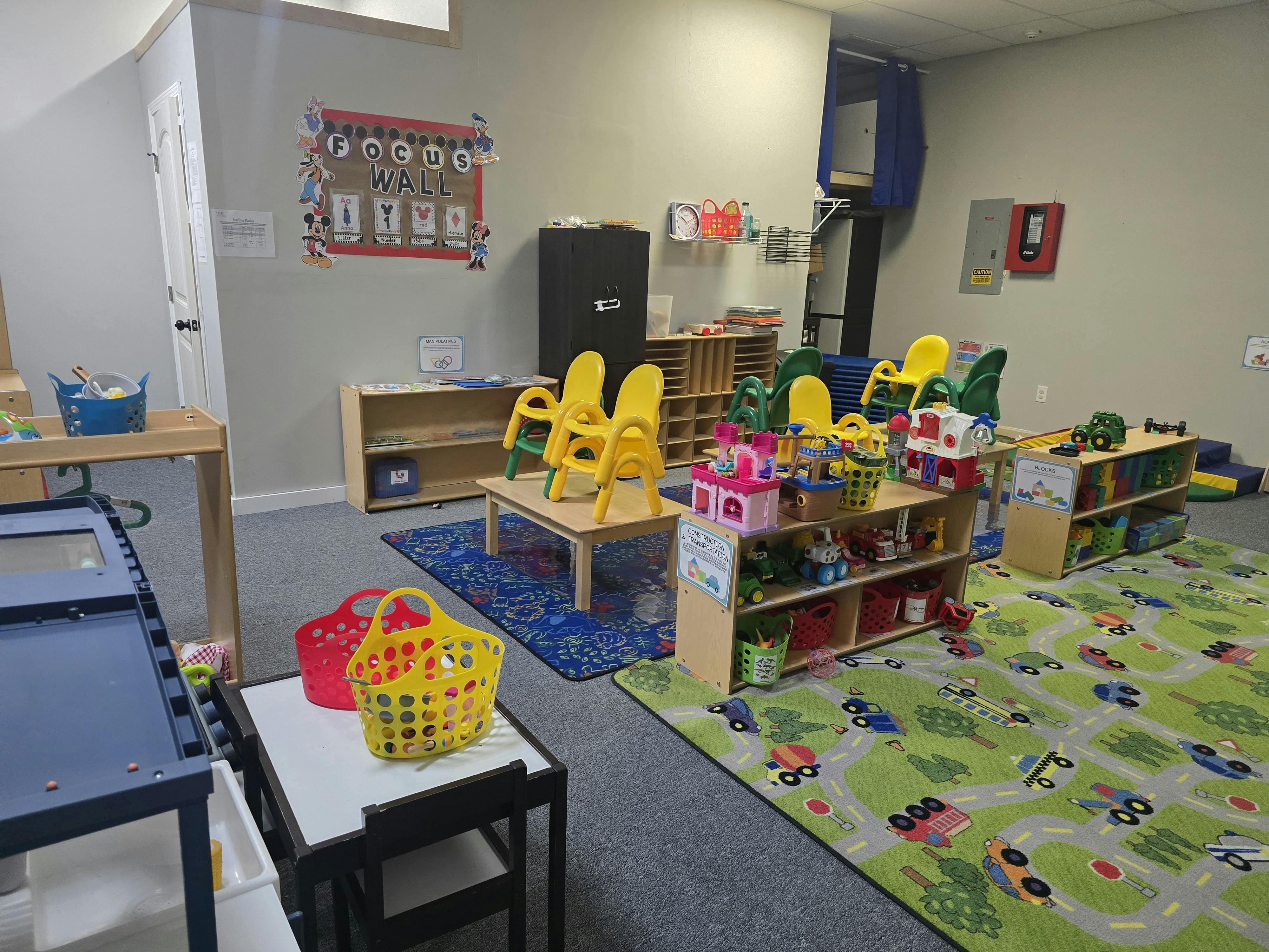 A classroom with small tables, chairs, and shelves with toys
