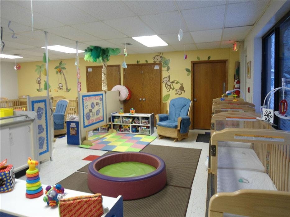 A colorful nursery room with multiple cribs, a playmat, and a blue rocking chair