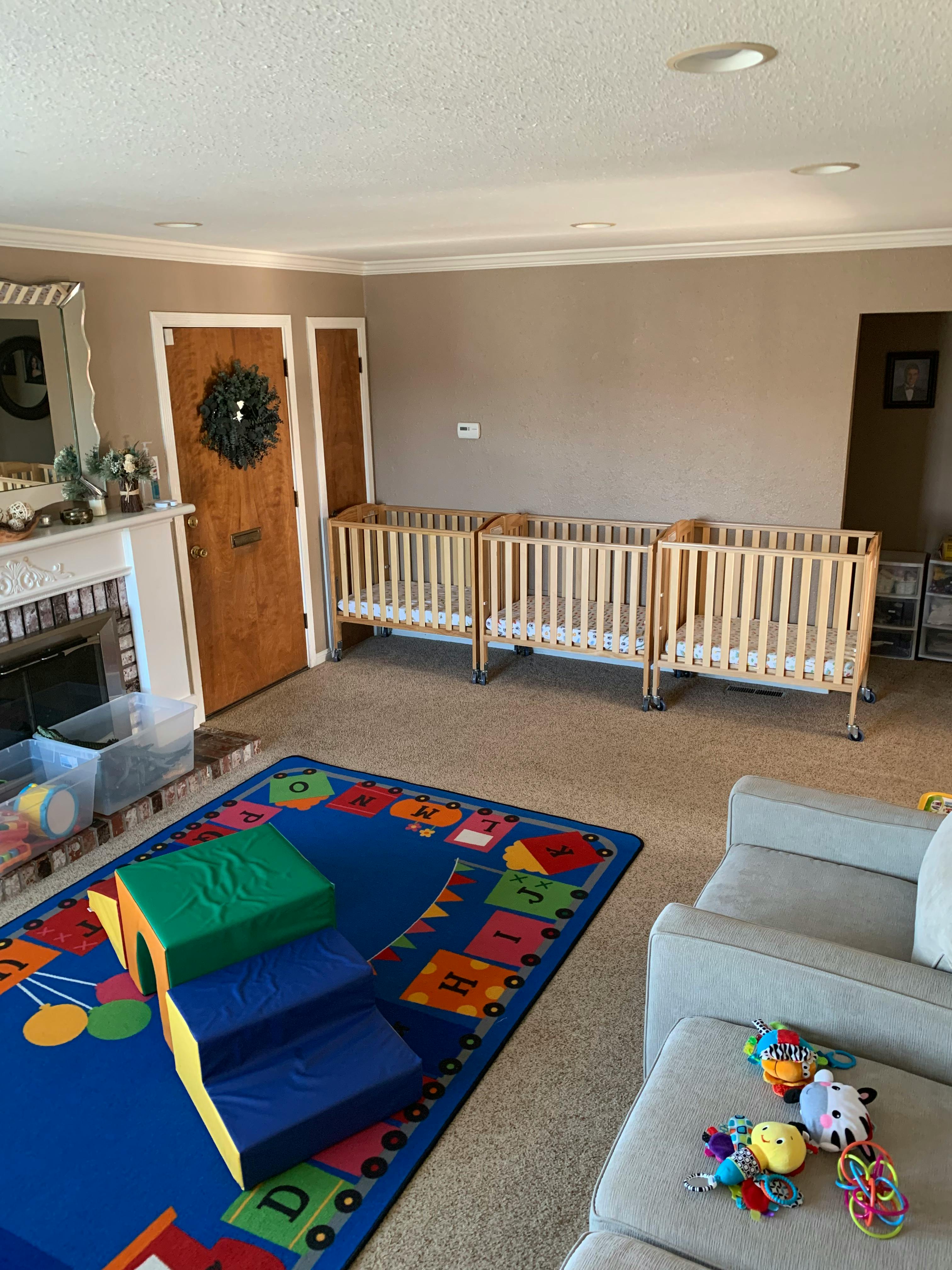 Three cribs in a room with a colorful playmat and soft play equipment