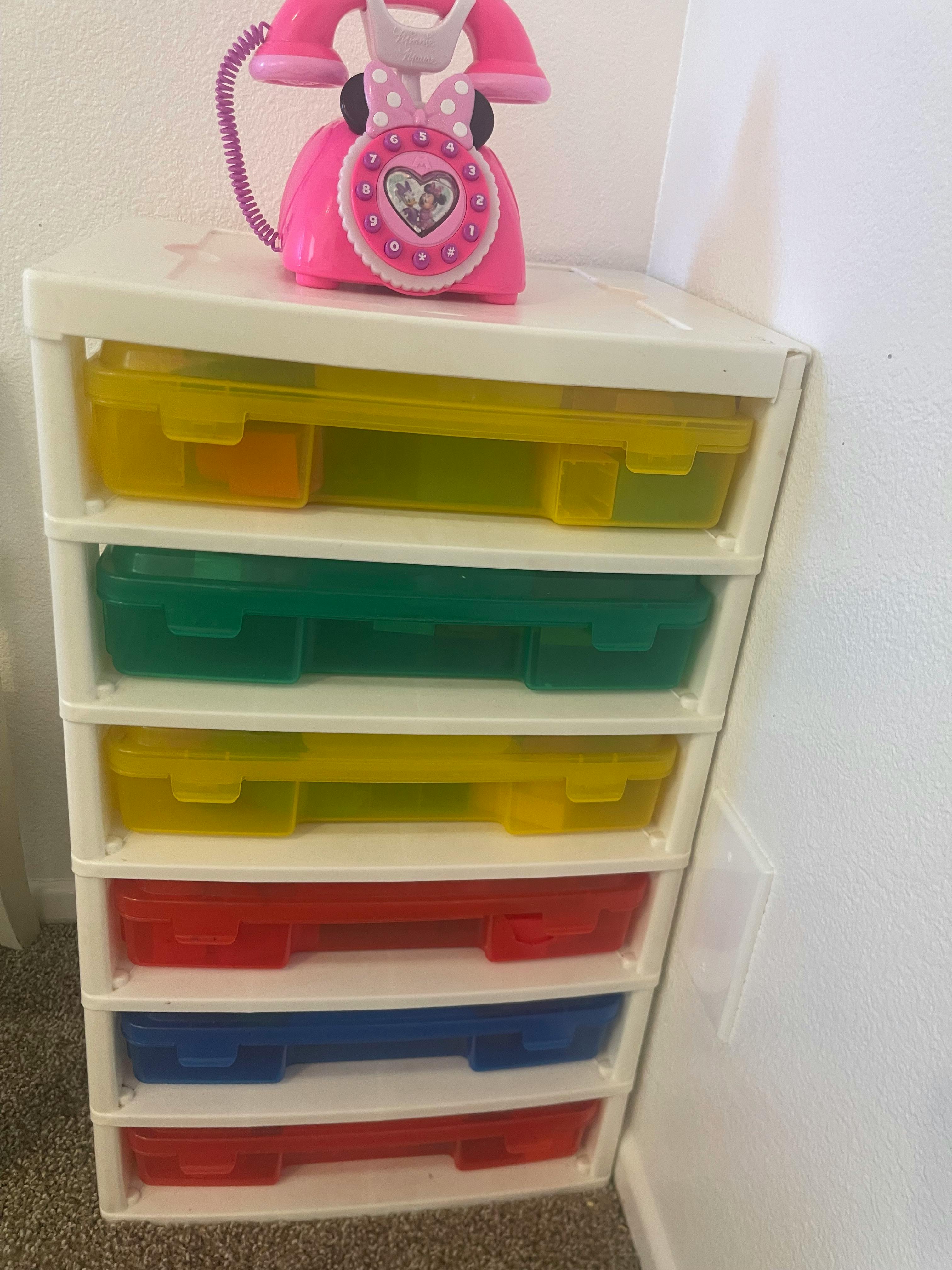 Pink toy telephone on top of a white storage unit with colorful drawers