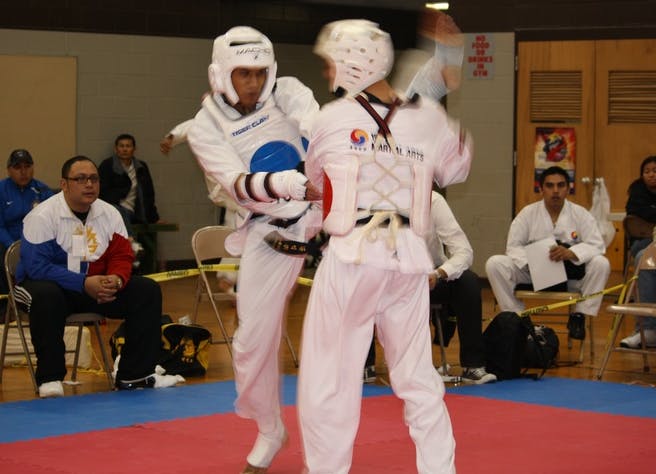 Two people in white taekwondo uniforms and headgear sparring