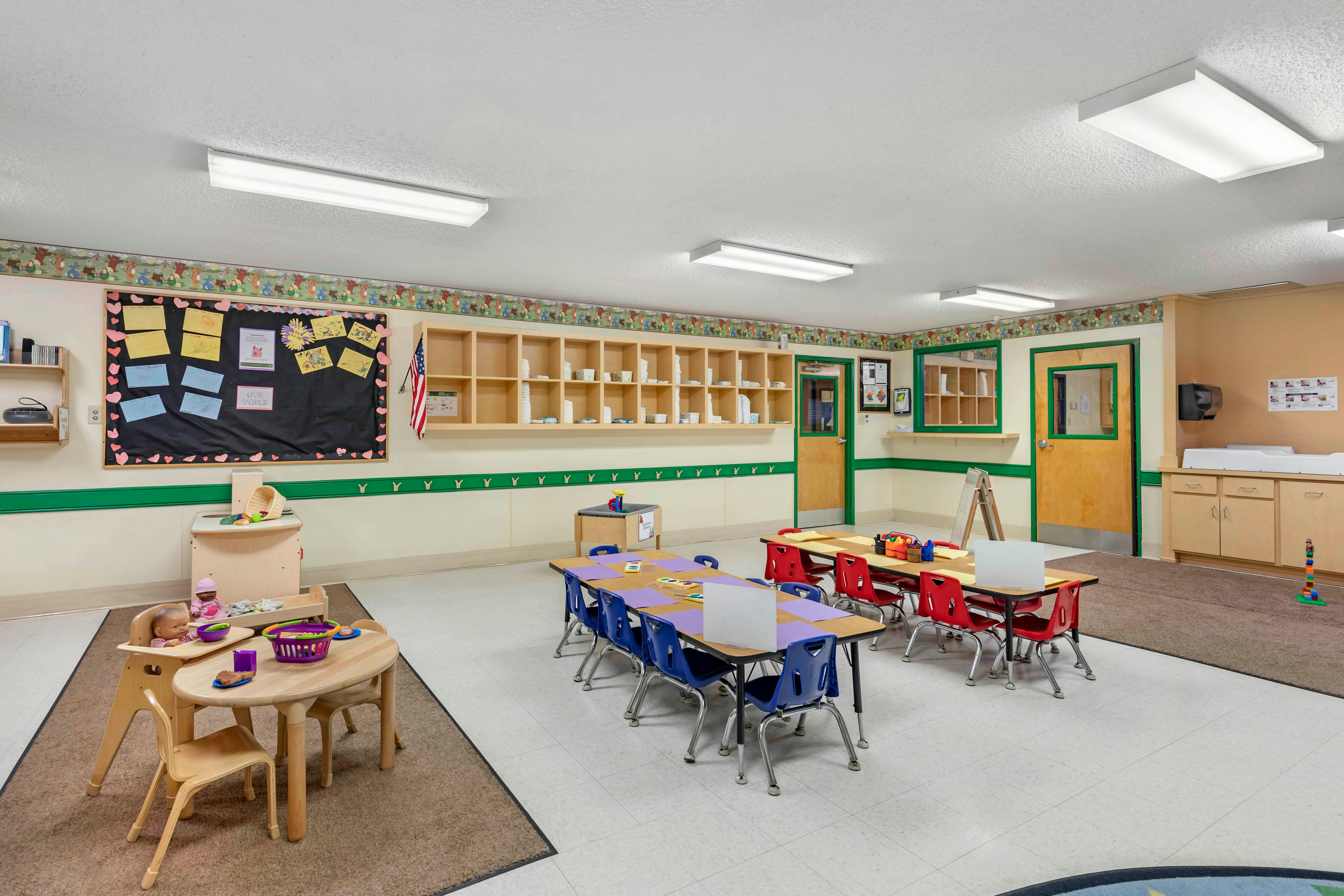 Classroom with tables, chairs, cubbies, a changing station, and bulletin board