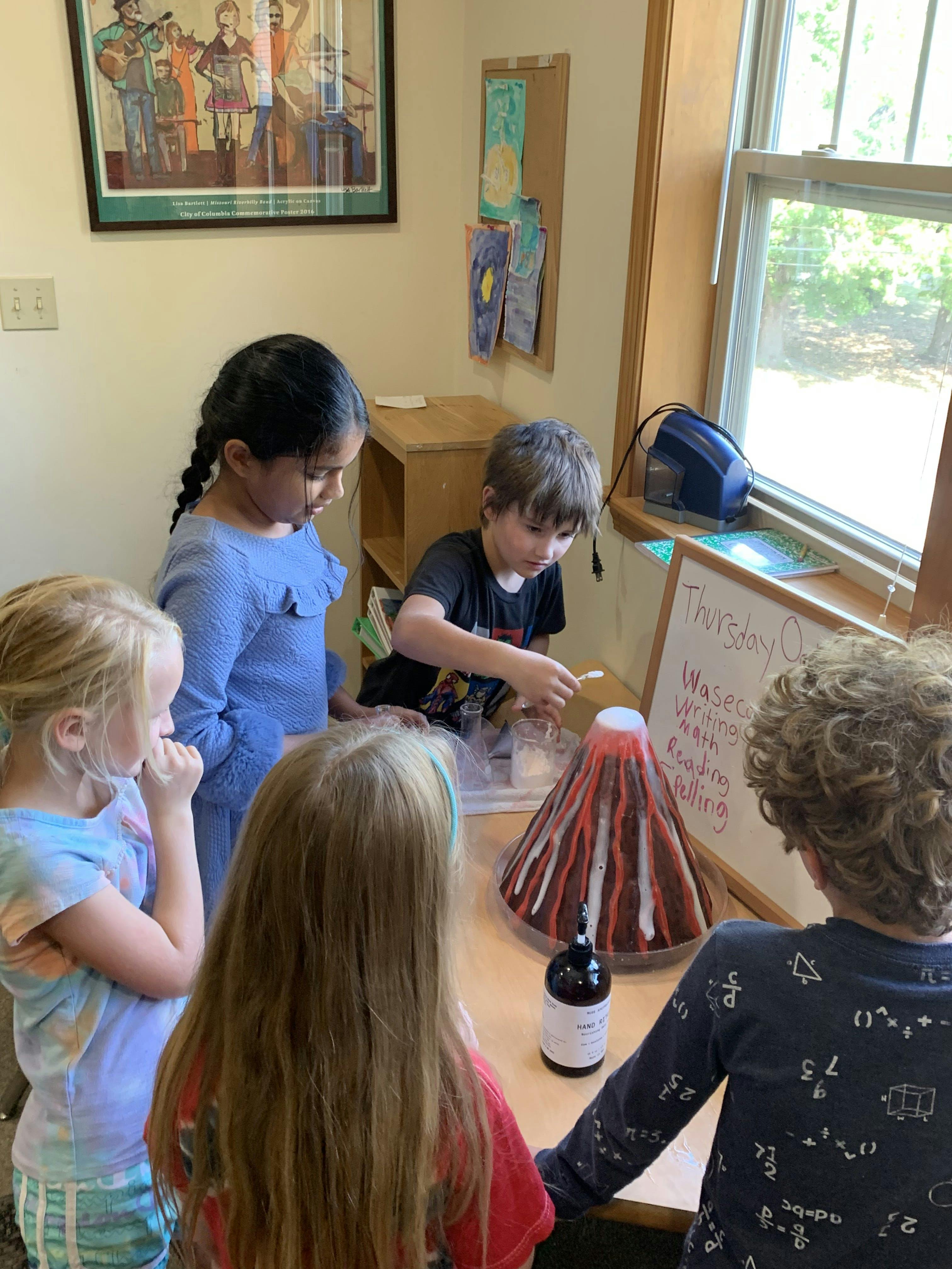 Children gathered around a table watching a volcano science experiment