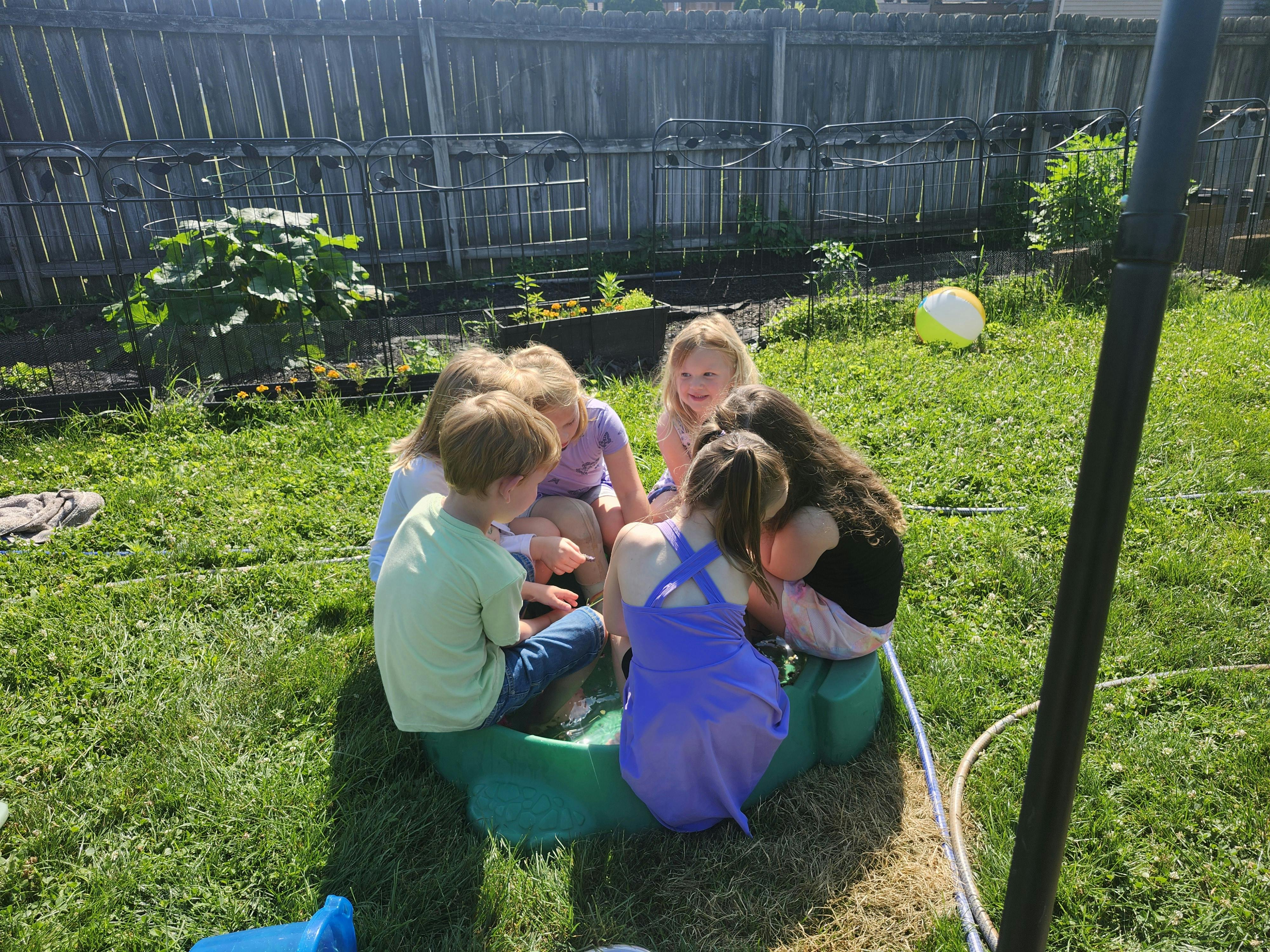 Group of children sitting in a green play structure in a grassy yard