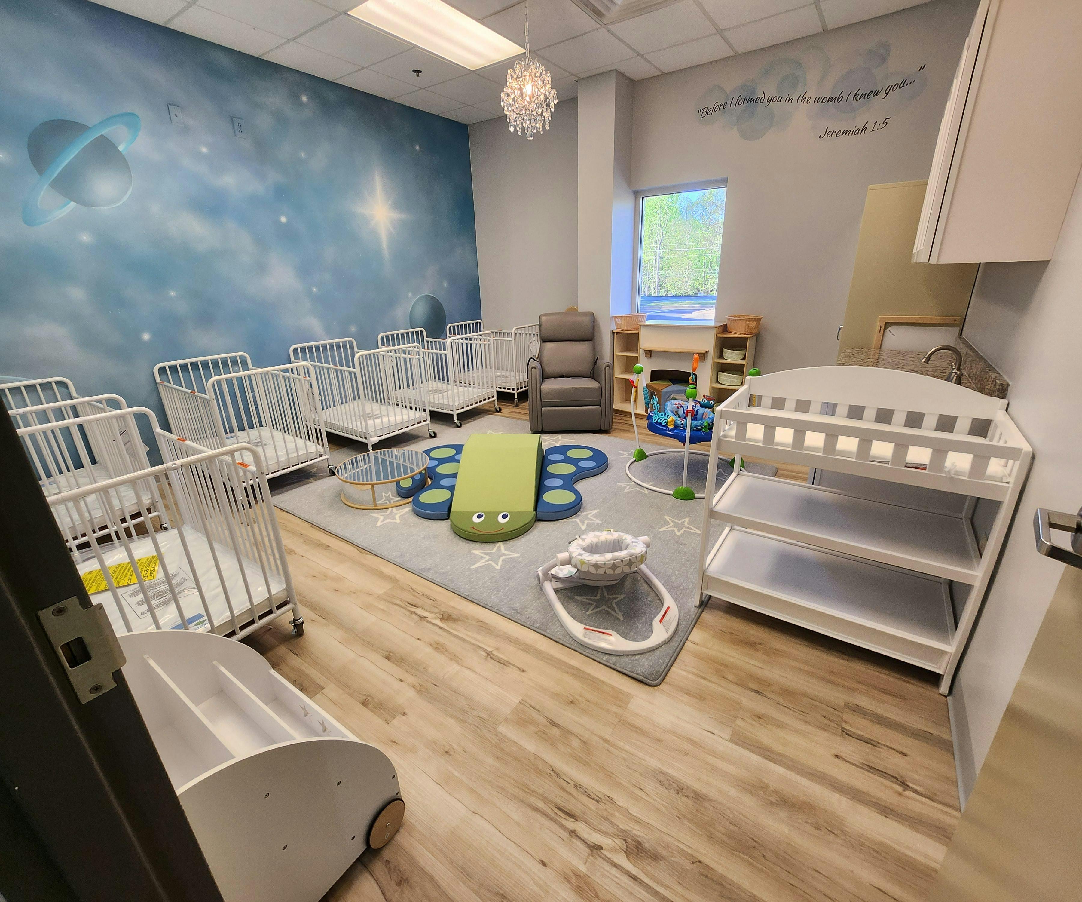 Room with multiple cribs, a changing table, and play mats on a rug