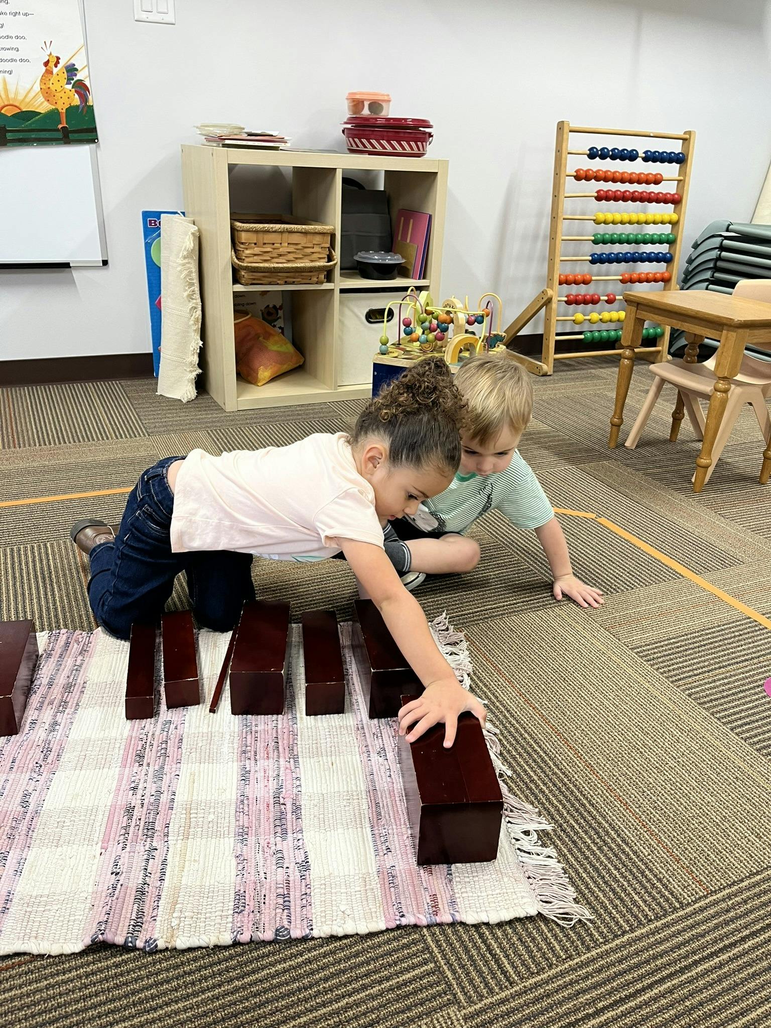 Two children playing with wooden blocks on a rug in a classroom