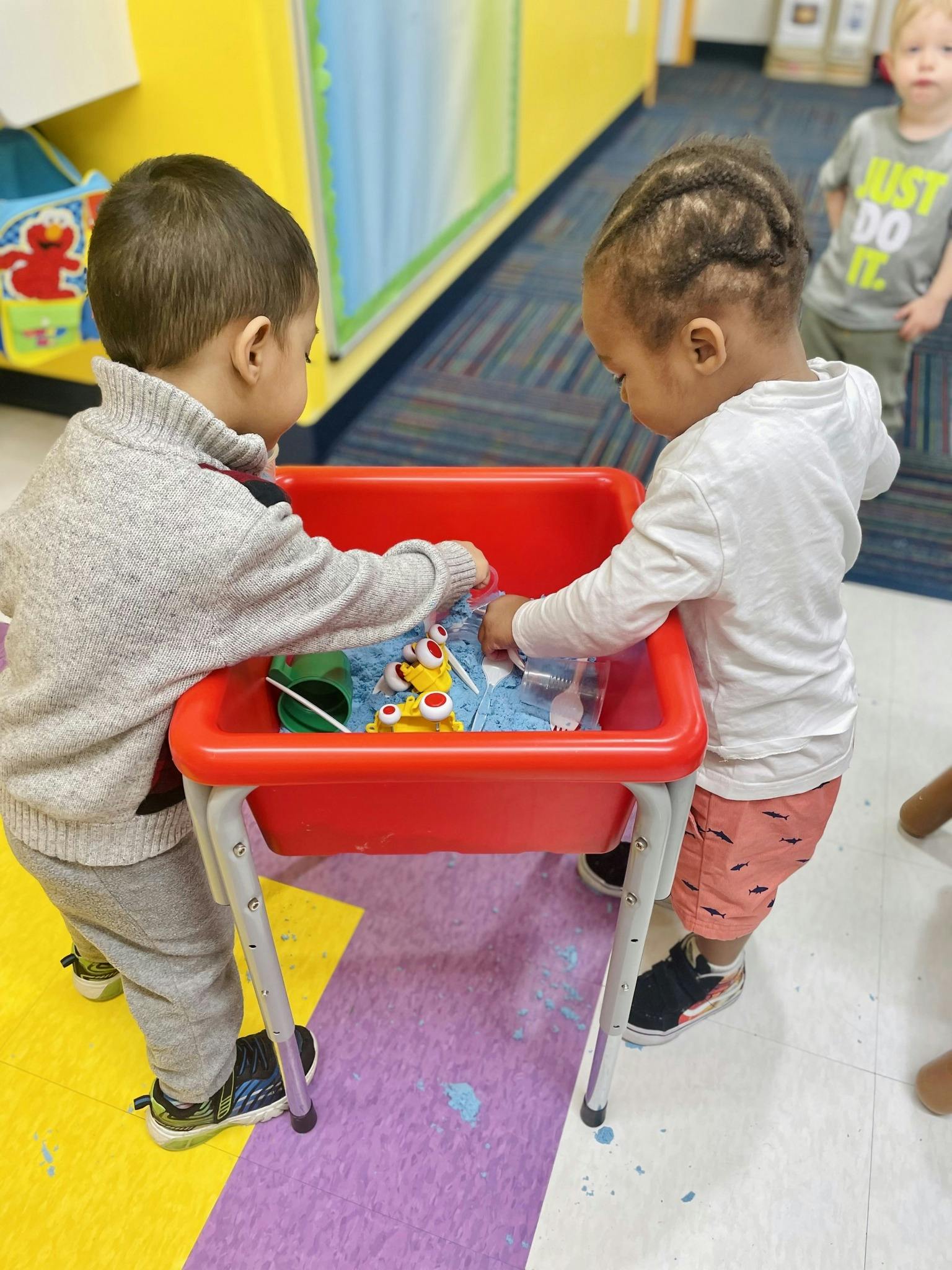 Two children playing with toys in a red sensory bin