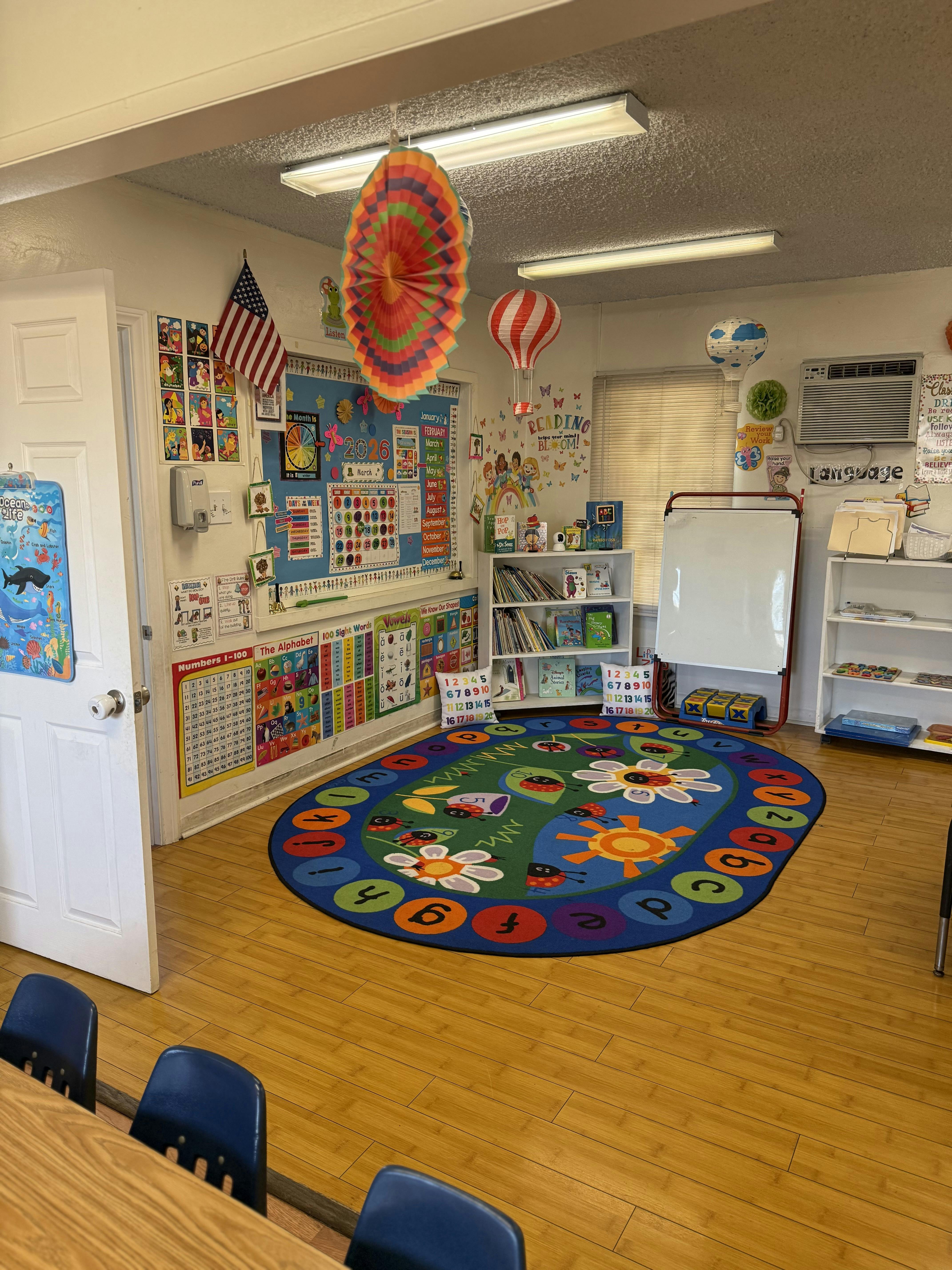 Colorful classroom with educational posters, a reading nook, and a circular rug with letters