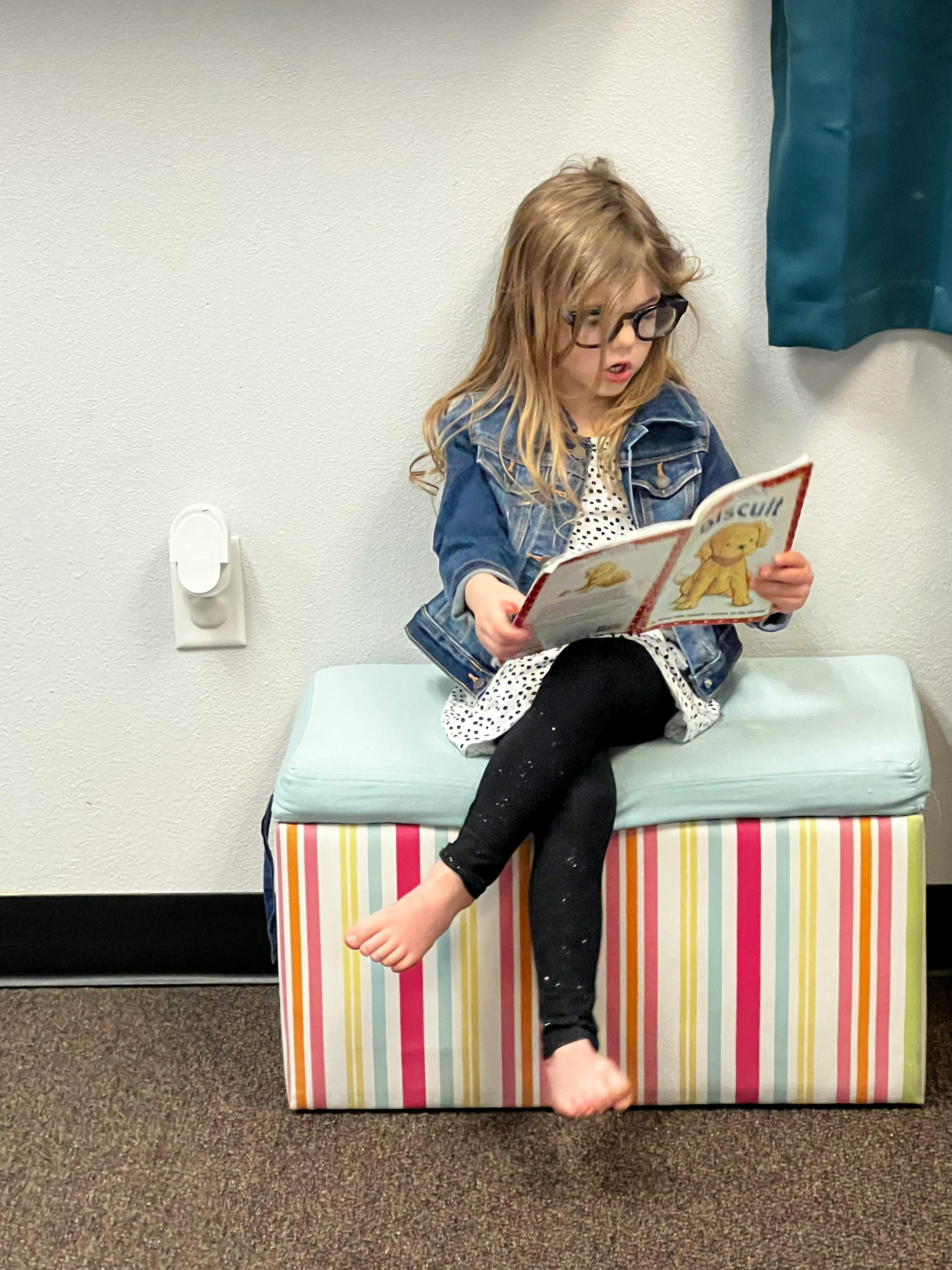 Child in glasses reading a book while sitting on a striped bench