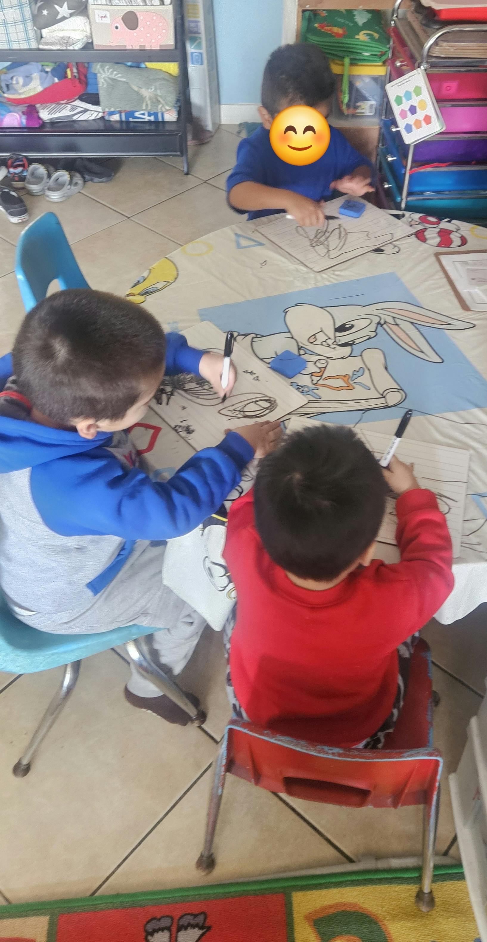 three children sitting at a table with coloring pages and markers