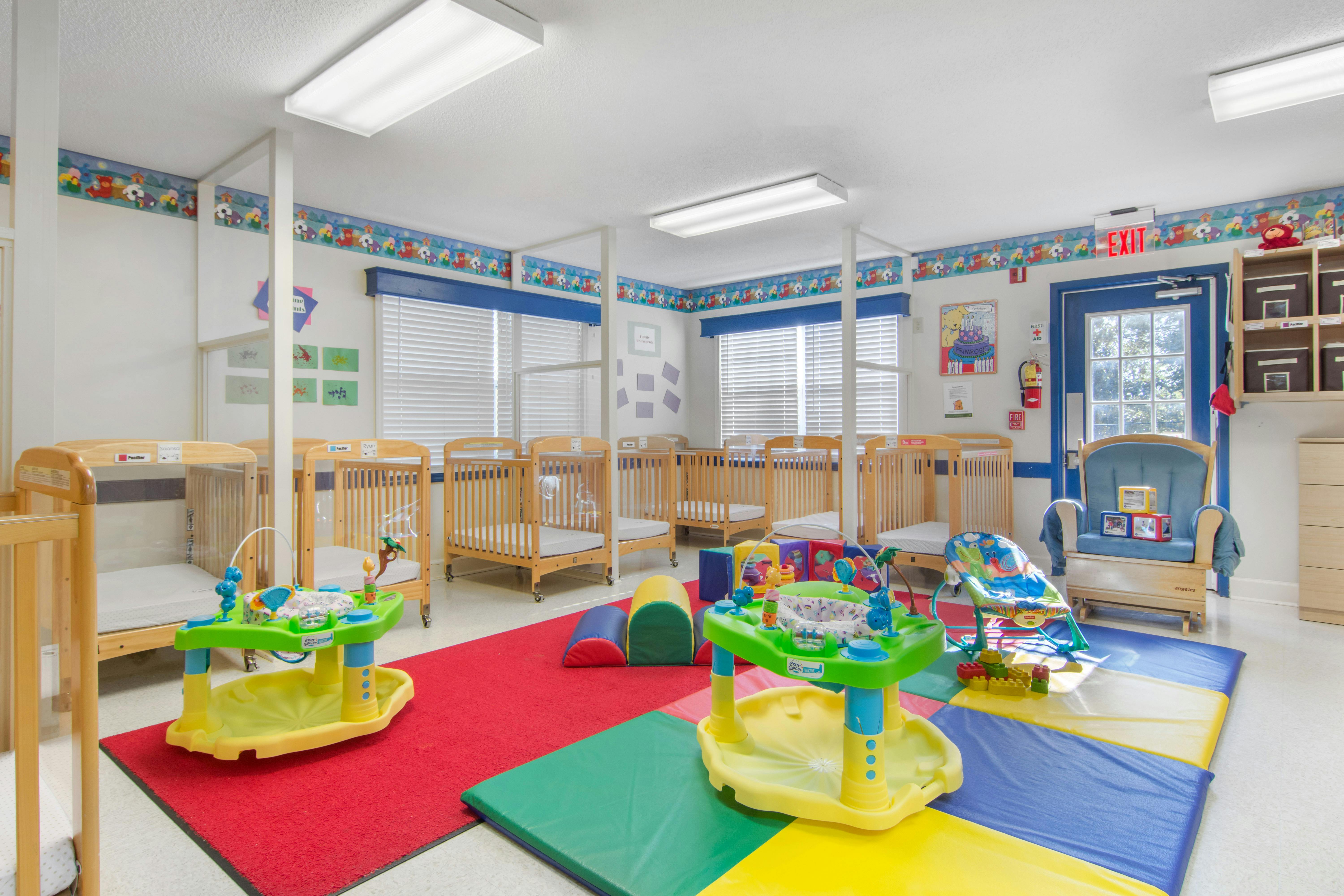 A childcare nursery with several cribs and colorful play mats on the floor