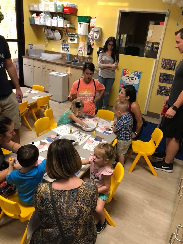Adults and children gathered around tables in a classroom