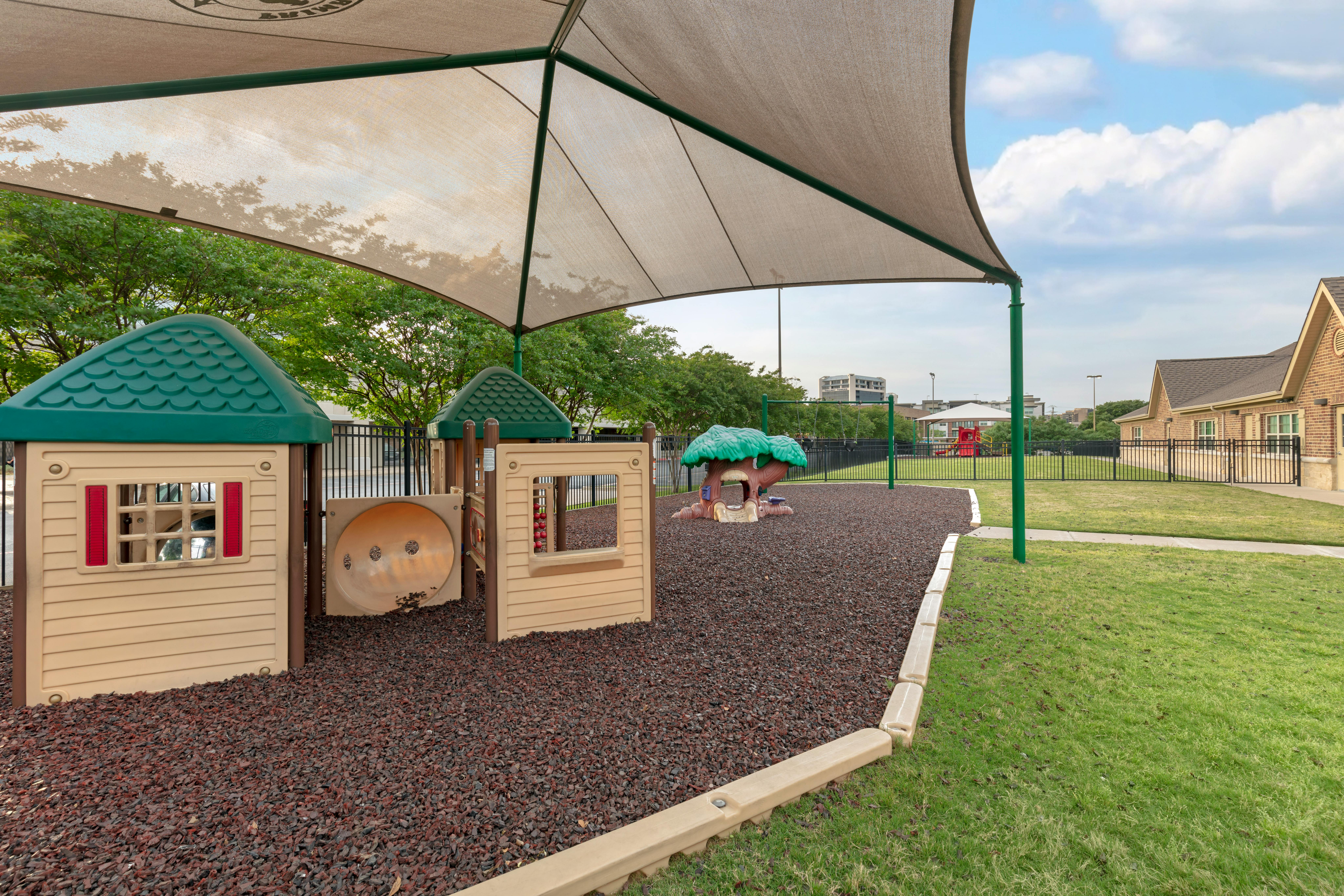 Playground with playhouses and a tree-shaped climber under a large sunshade