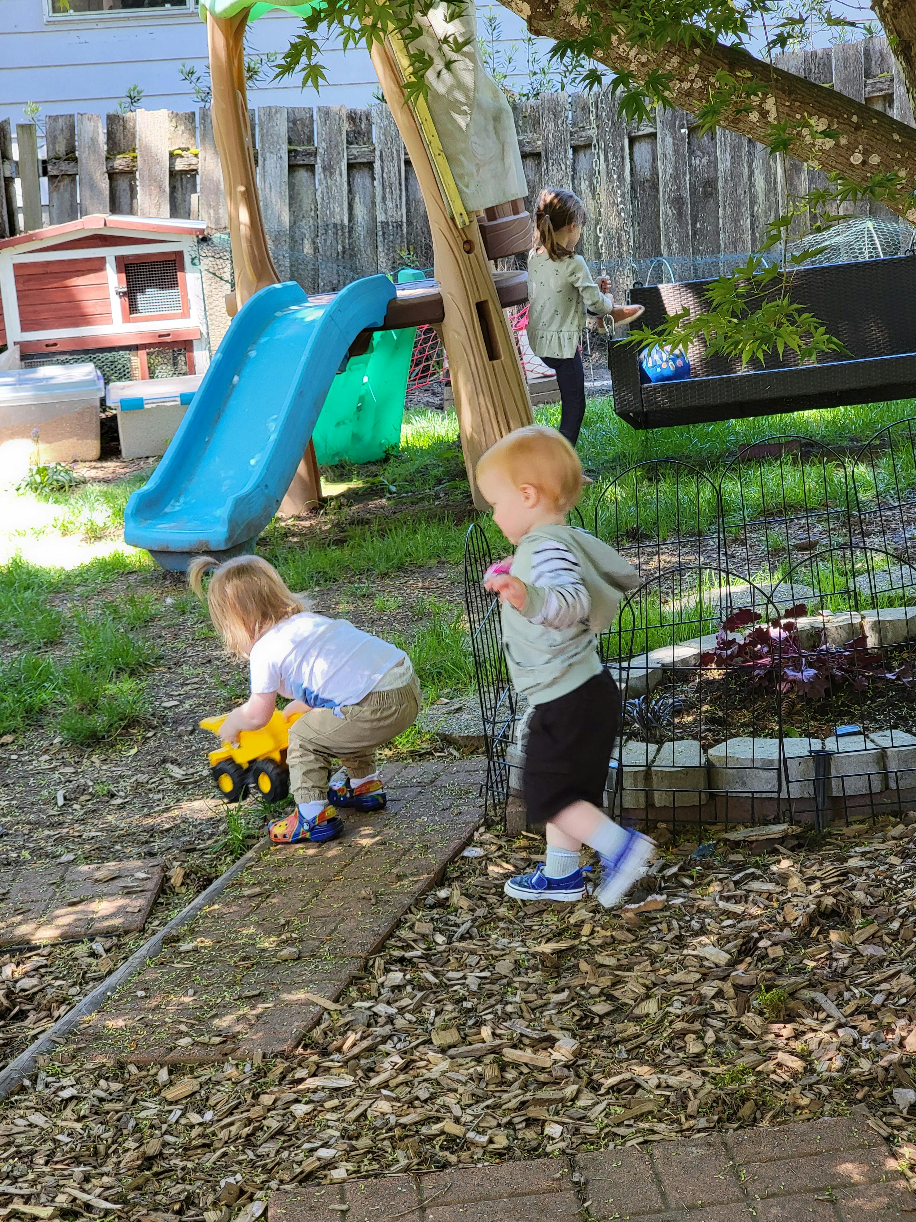 Three children playing in a backyard, one with a toy truck