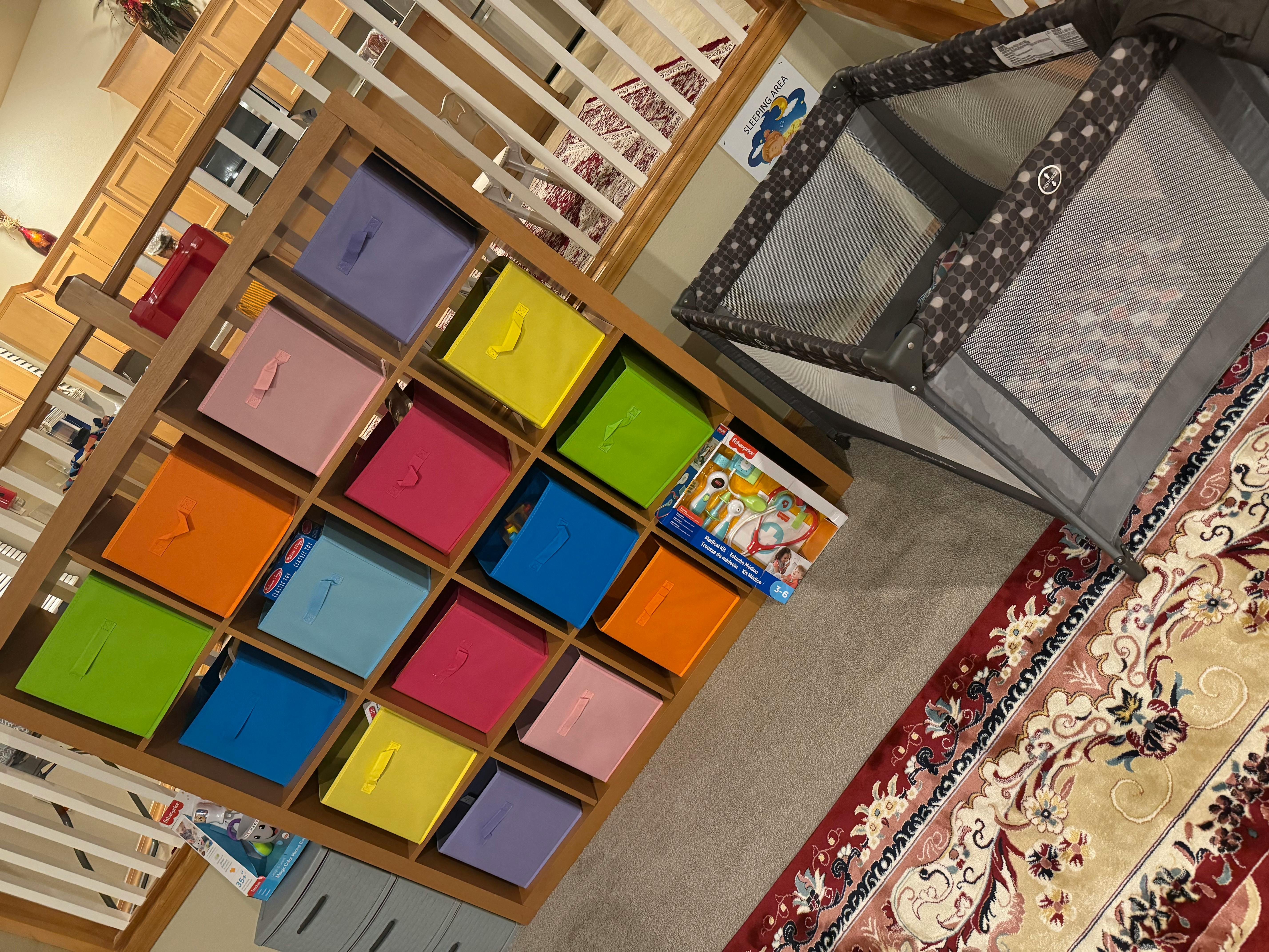 Storage unit with colorful bins next to a playpen and rug