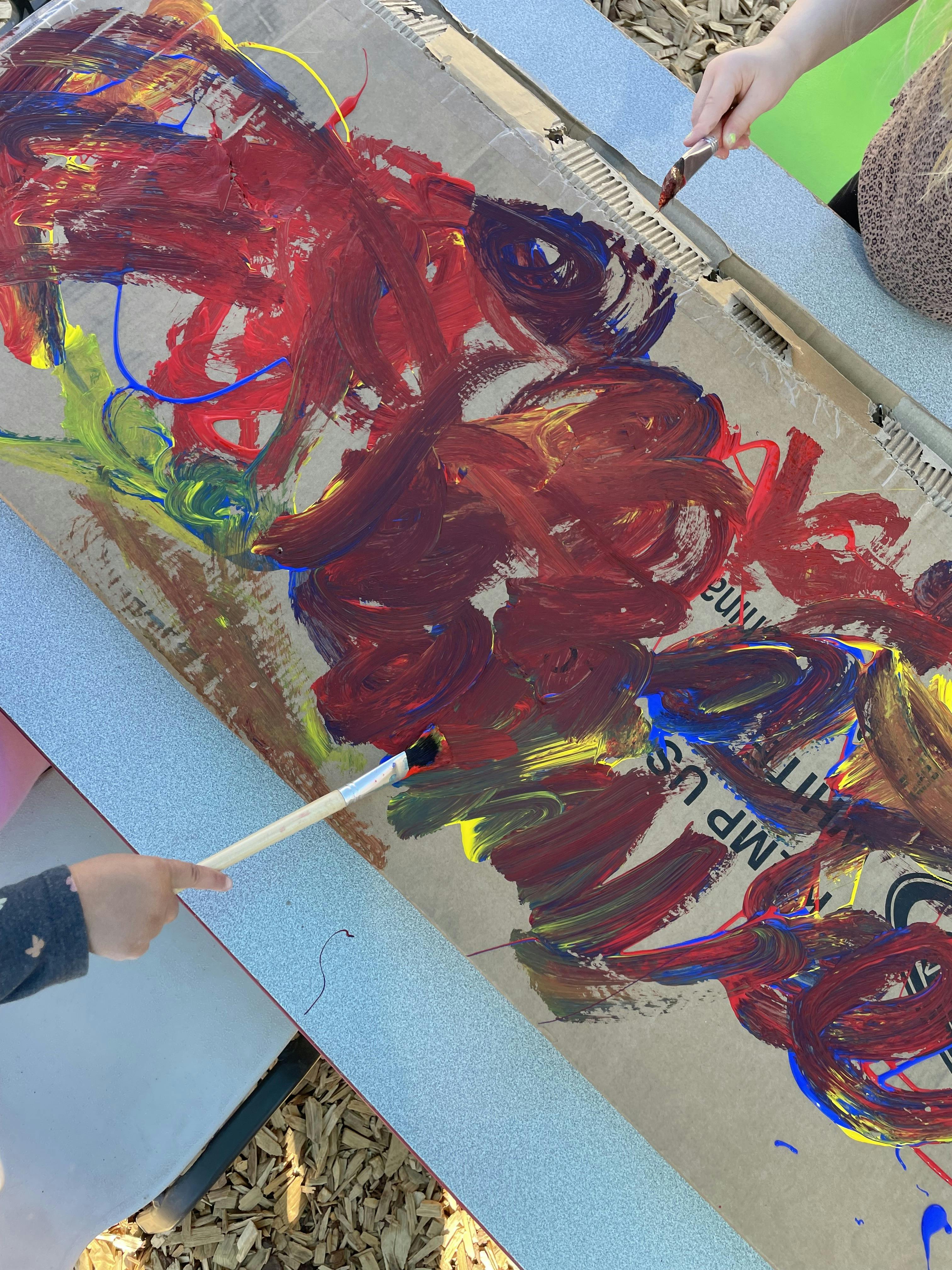 People using paintbrushes to paint on a piece of cardboard