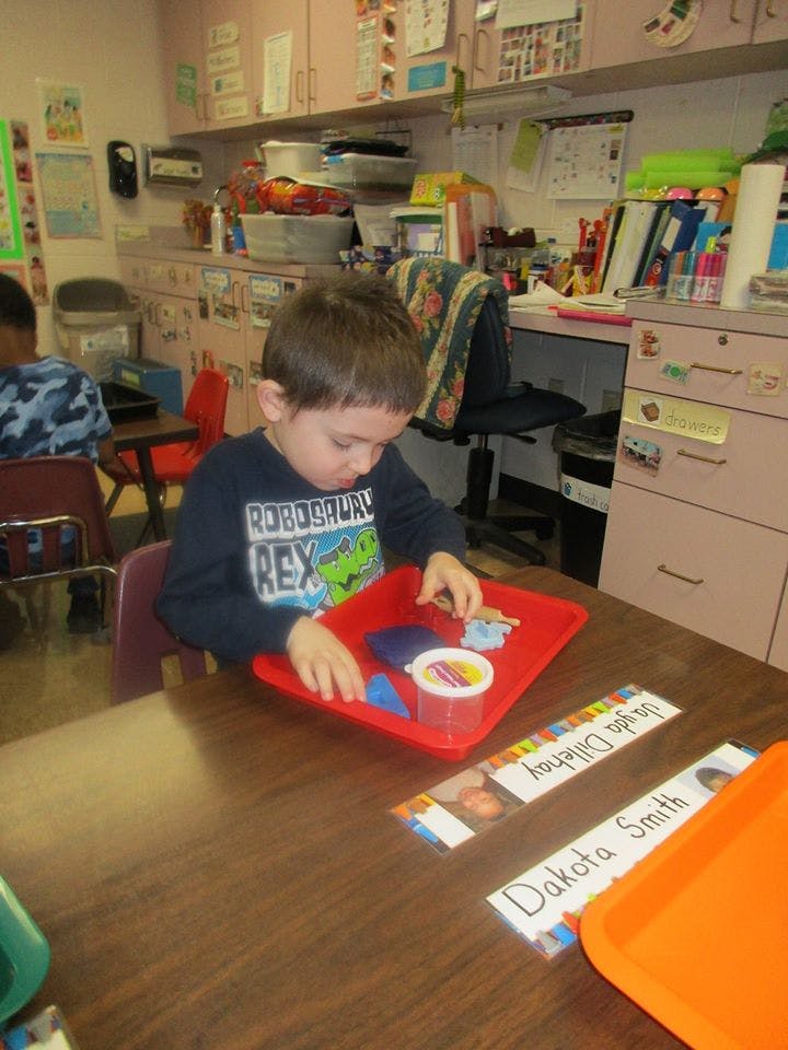 Child playing with items on a red tray at a table in a classroom