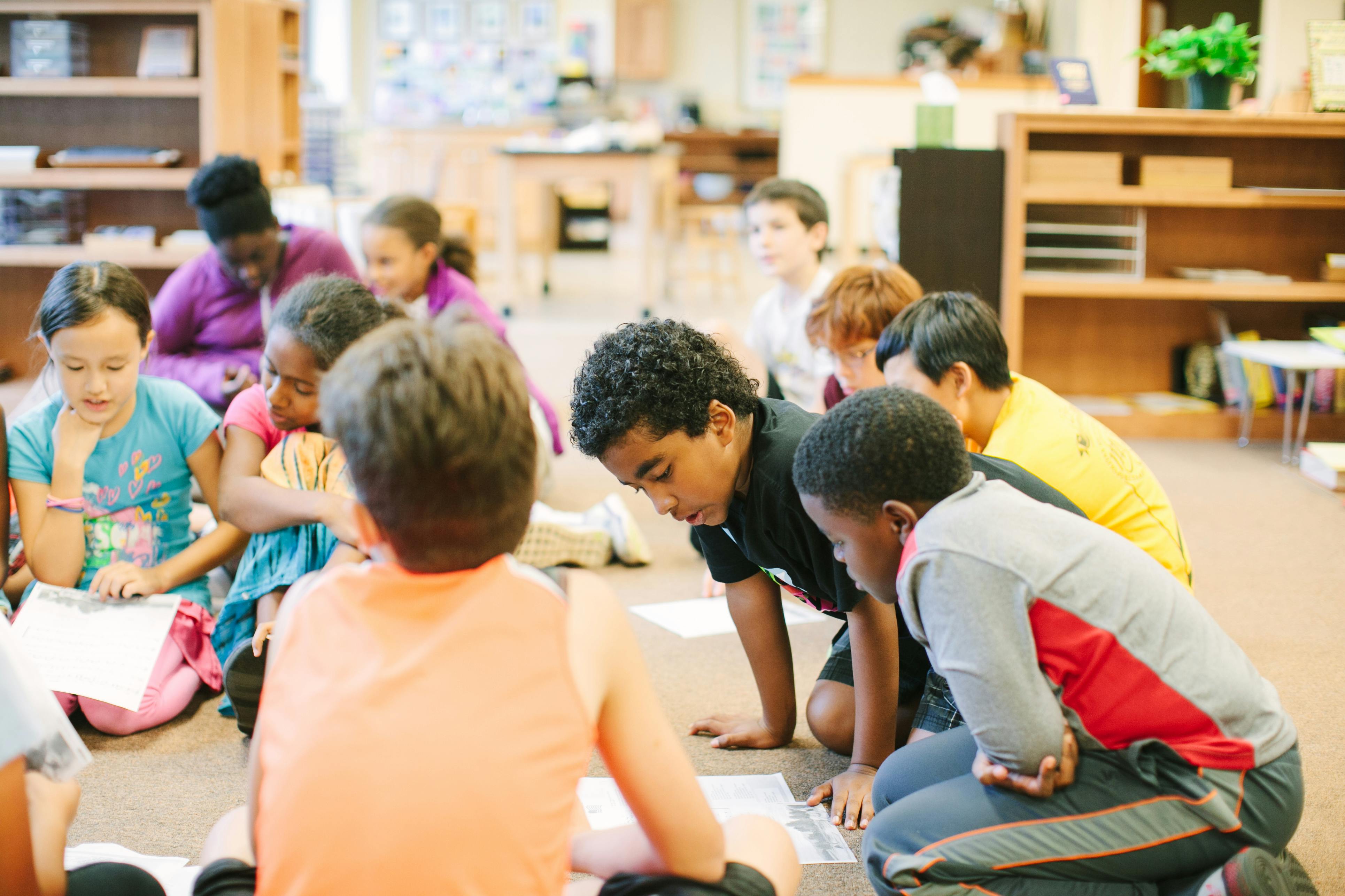 Children sitting on the floor looking at papers in a classroom