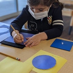 Child in mask drawing on paper at a table