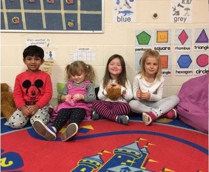Four children sitting on a rug in a classroom