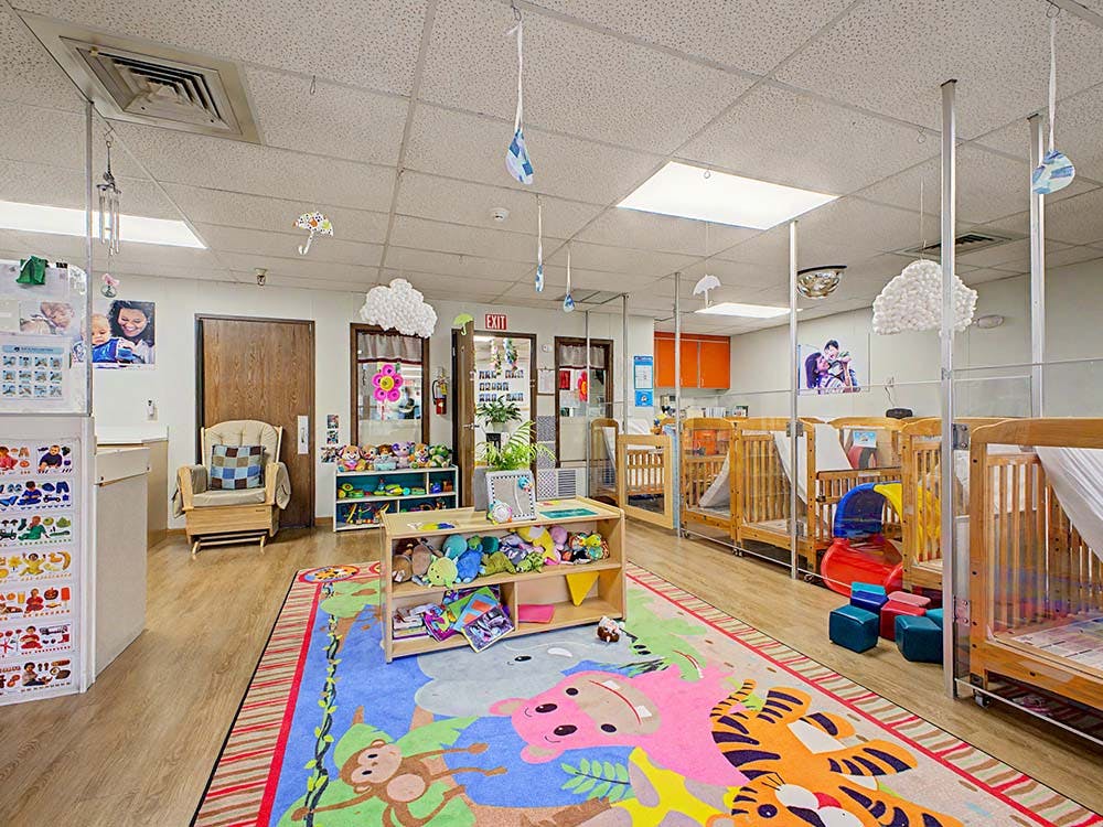 A childcare classroom with cribs, a colorful rug, and toys