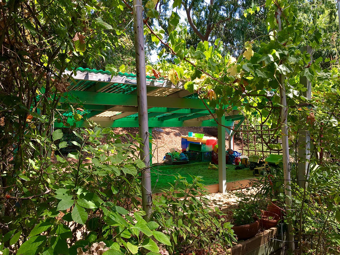 Outdoor shelter with green roof and play area visible through trees