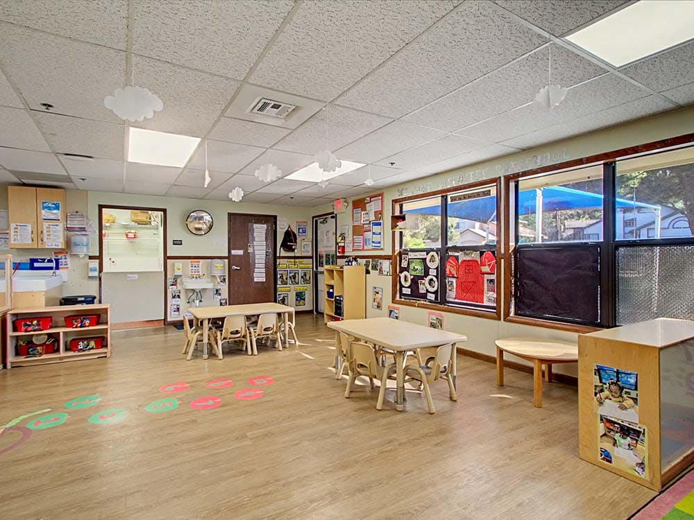 Empty classroom with small tables and chairs, windows, and storage units