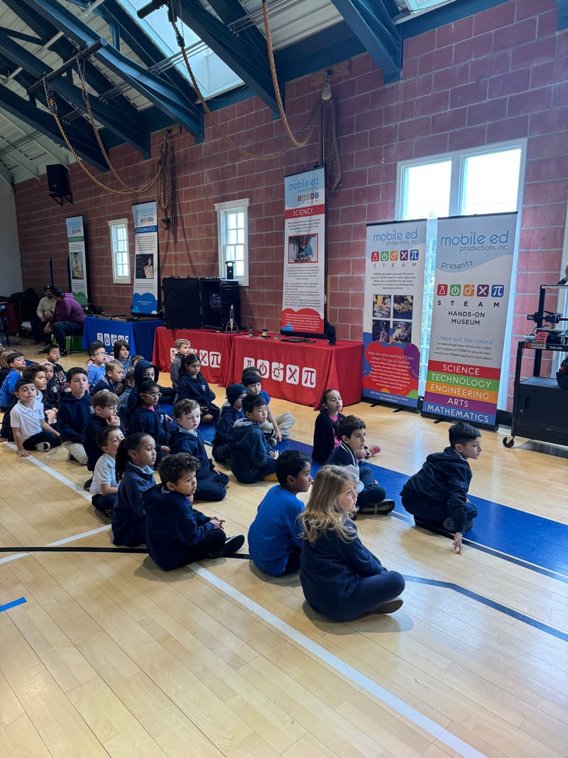 Children sitting on a wooden floor, facing presentation banners about STEAM education