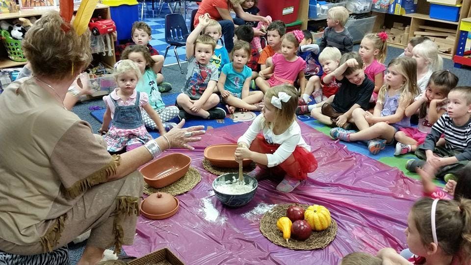 Person with feather headband teaching children in a classroom