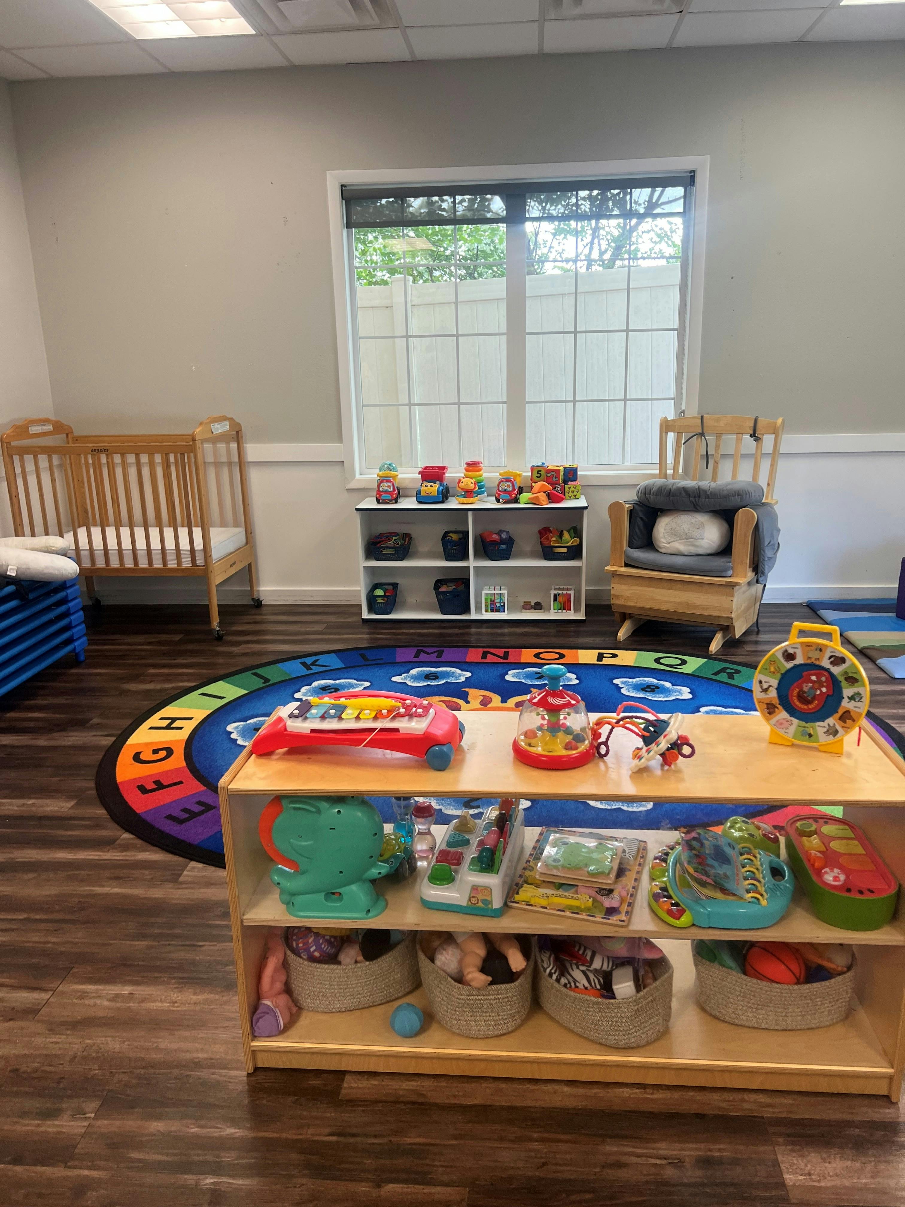 Childcare room with toys, a crib, and alphabet rug