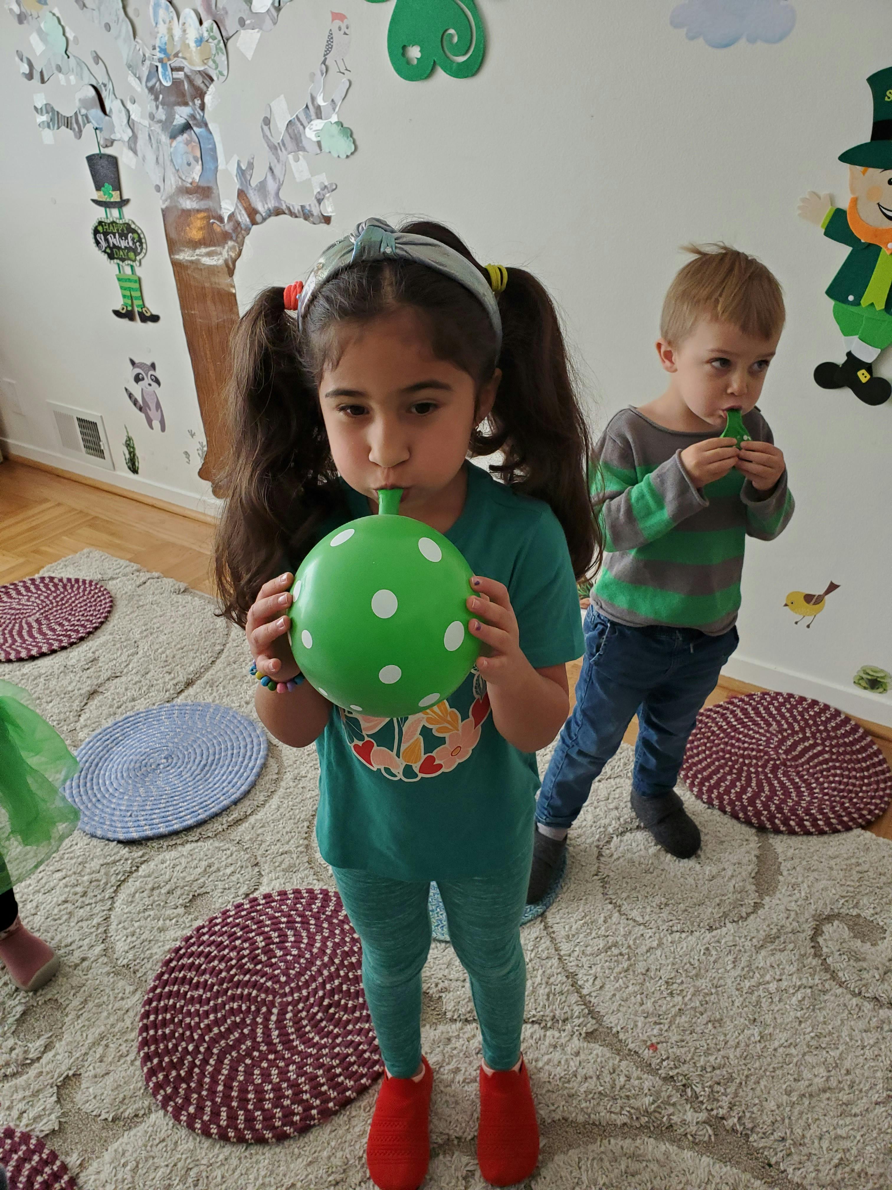Child blowing up a green balloon with white polka dots