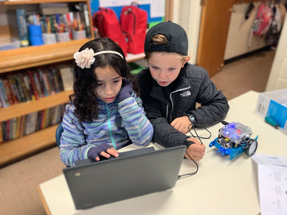 Two children looking at a laptop with a small robot connected to it