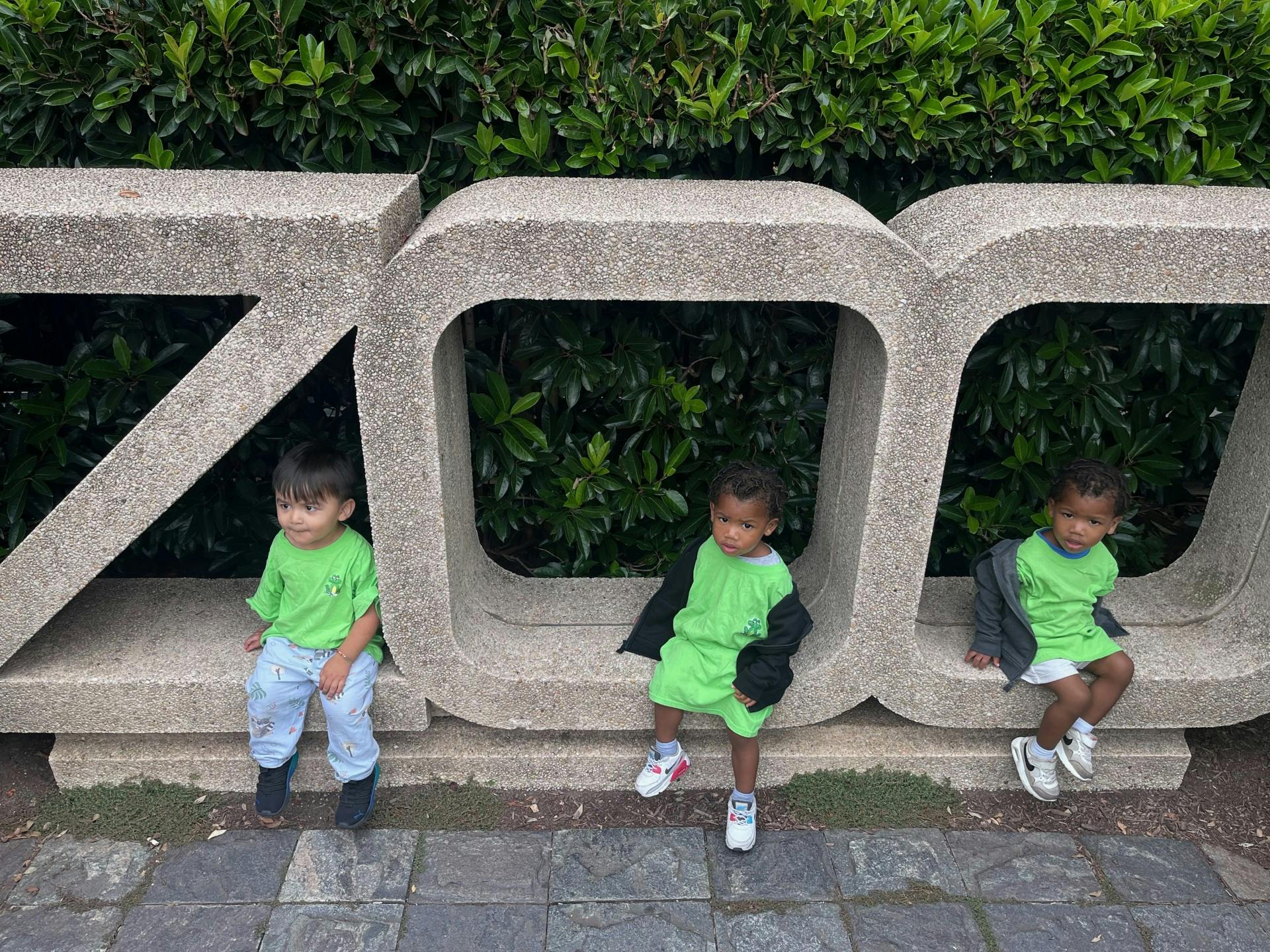 Three children sitting on large concrete letters spelling ZOO