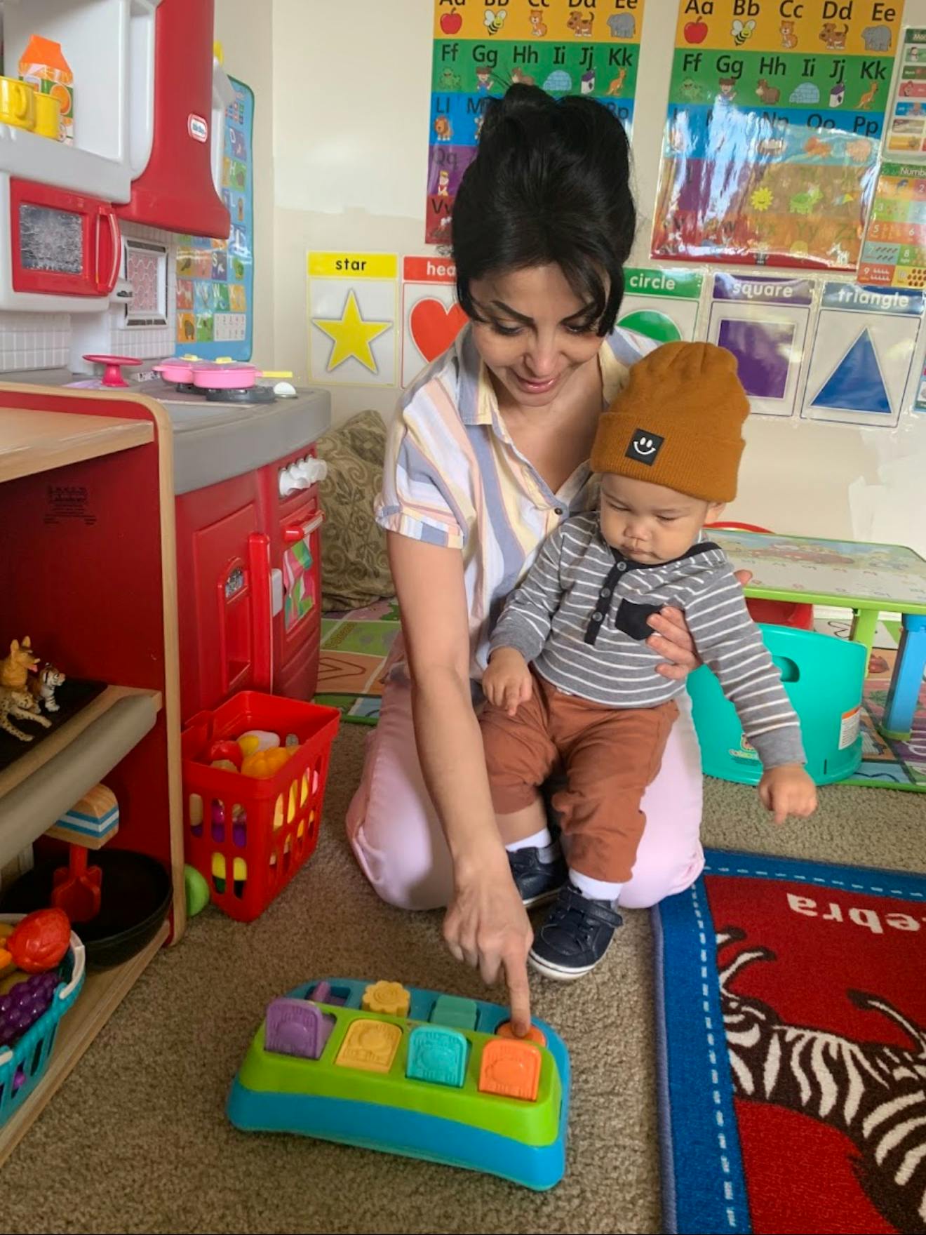 Person holding a child and pointing at a toy in a classroom