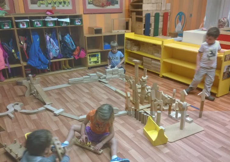 Three children playing with wooden blocks on a classroom floor