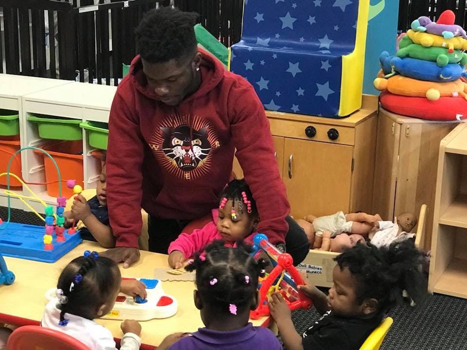 Person in red hoodie with children playing with toys at a table