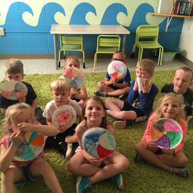 Group of children sitting on a rug holding paper plate crafts