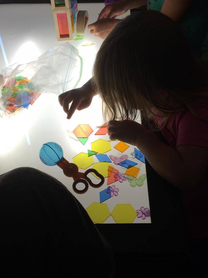 Child playing with colorful translucent shapes on a light table