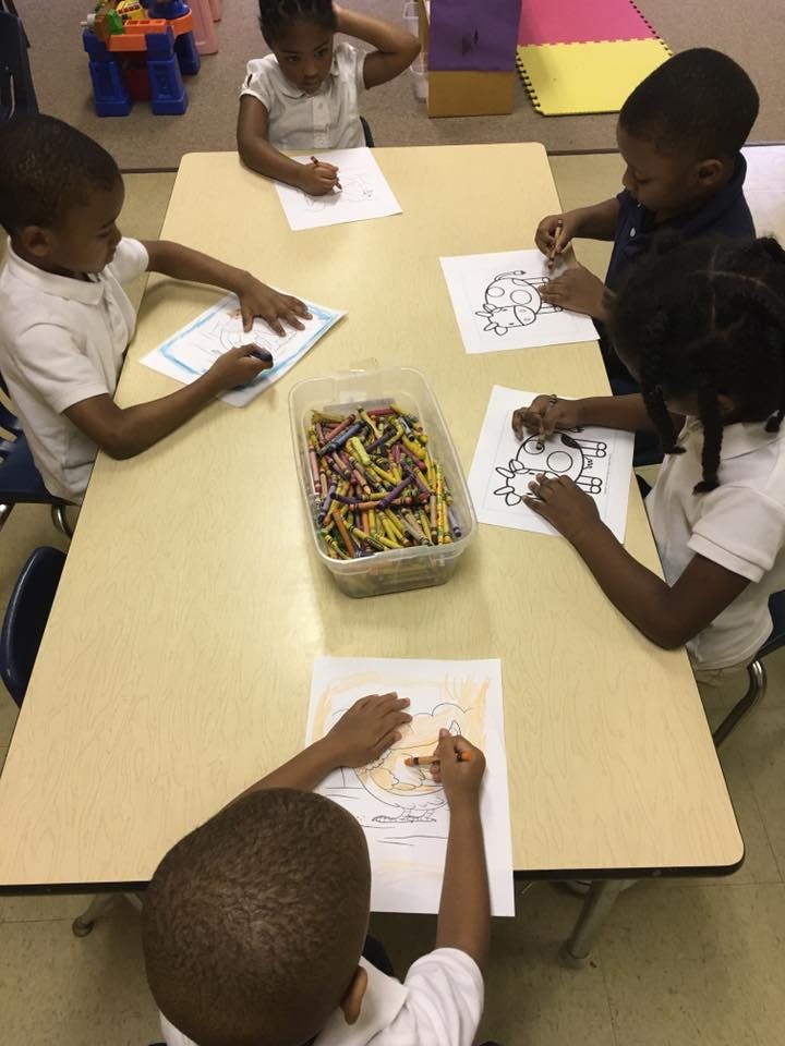 Children coloring at a table with a container of crayons