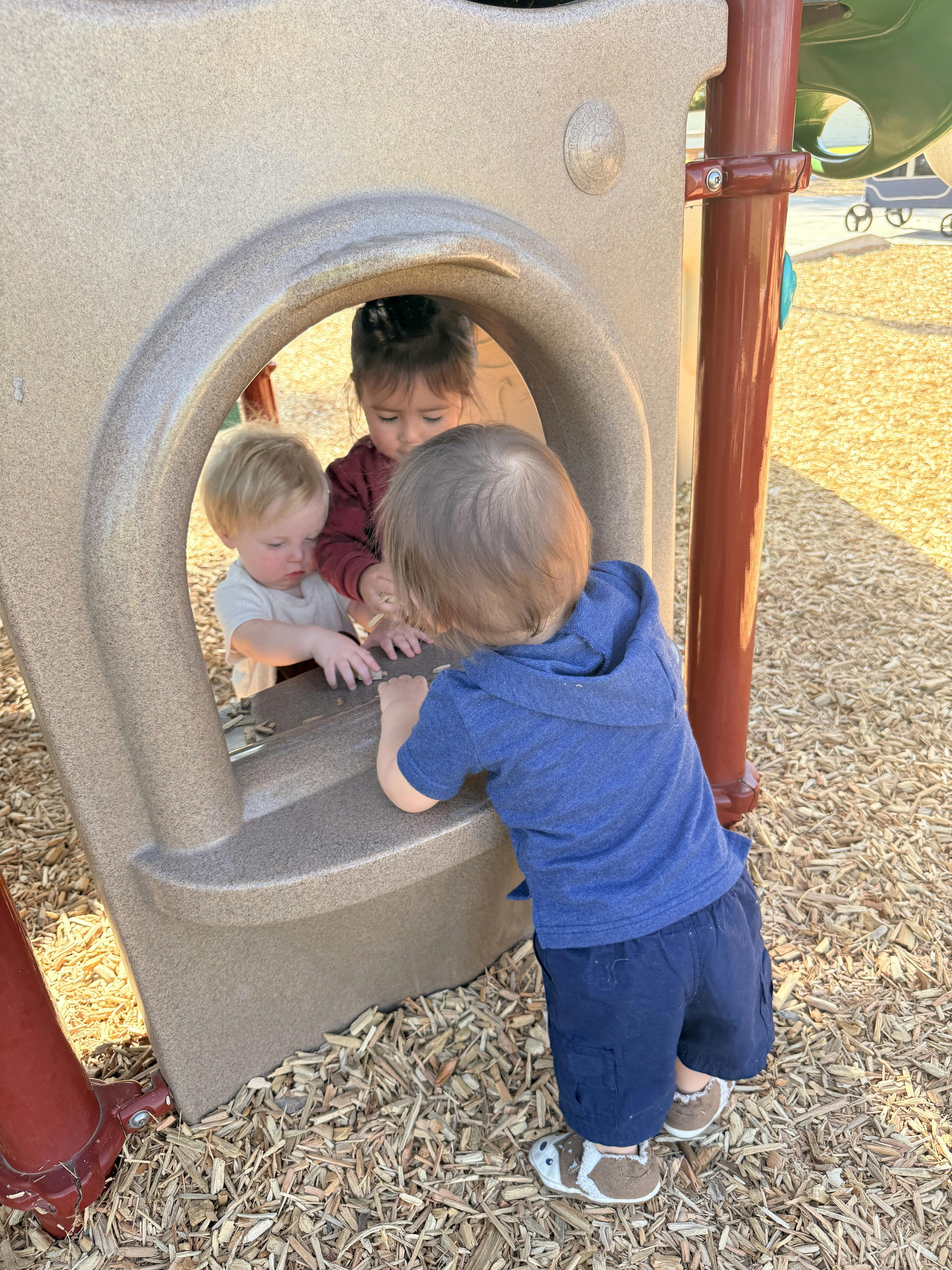 Three young children playing in a window on a playground structure