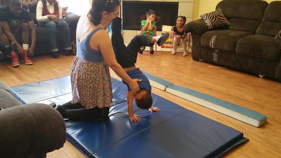 Person helping a child do a handstand on a mat
