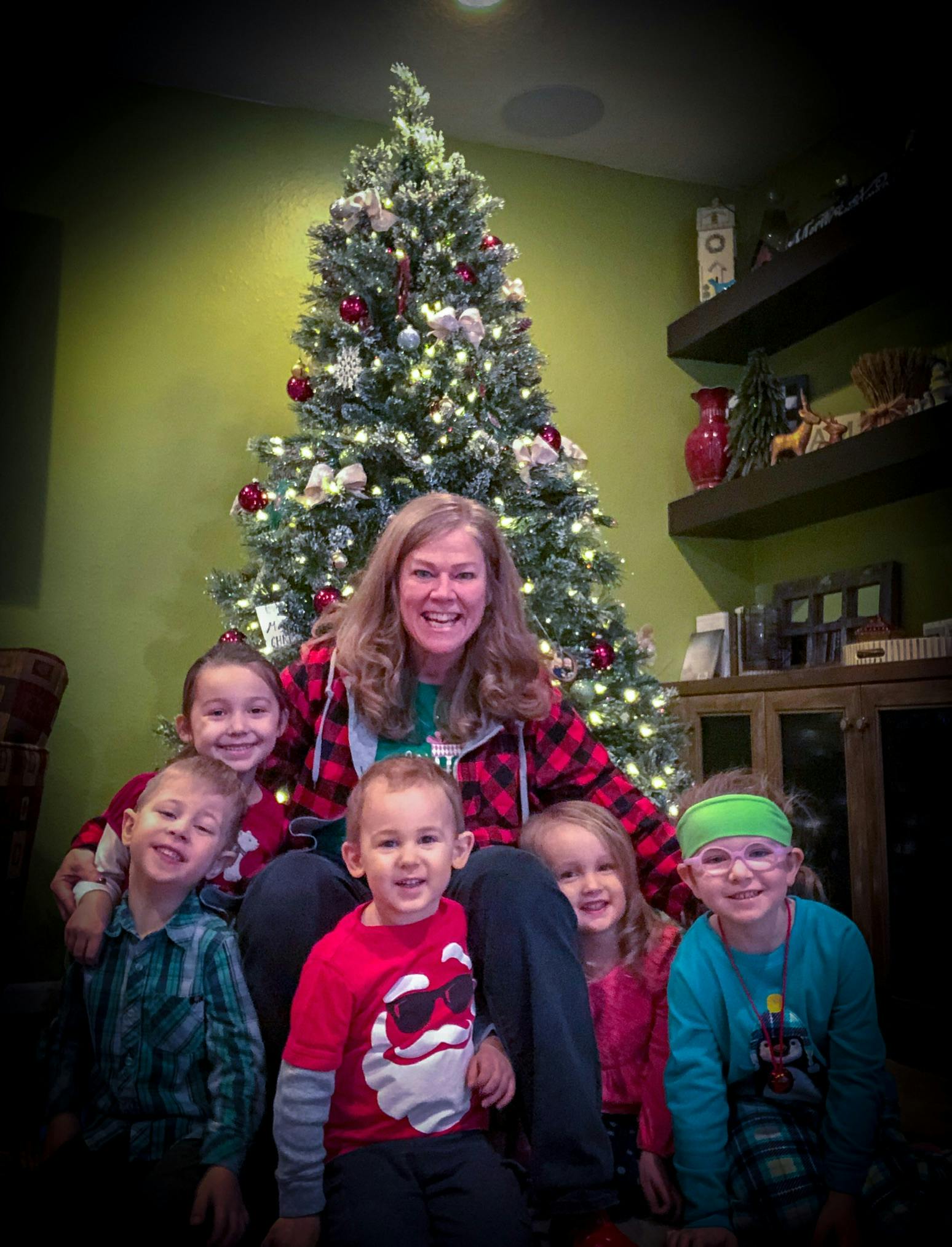 Person sitting in front of a Christmas tree with five children around them