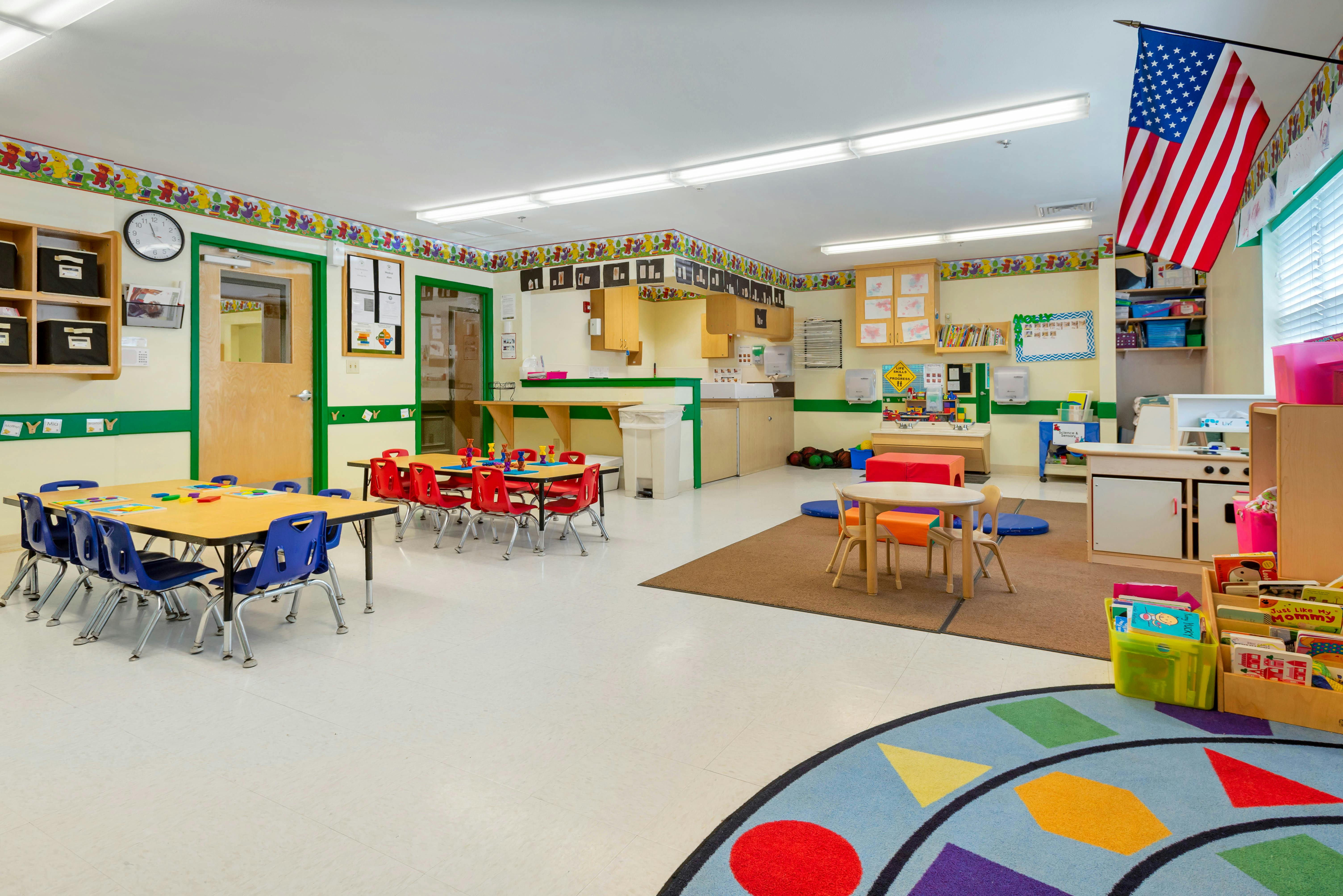 Classroom with small tables and chairs, an American flag, and children's activity areas